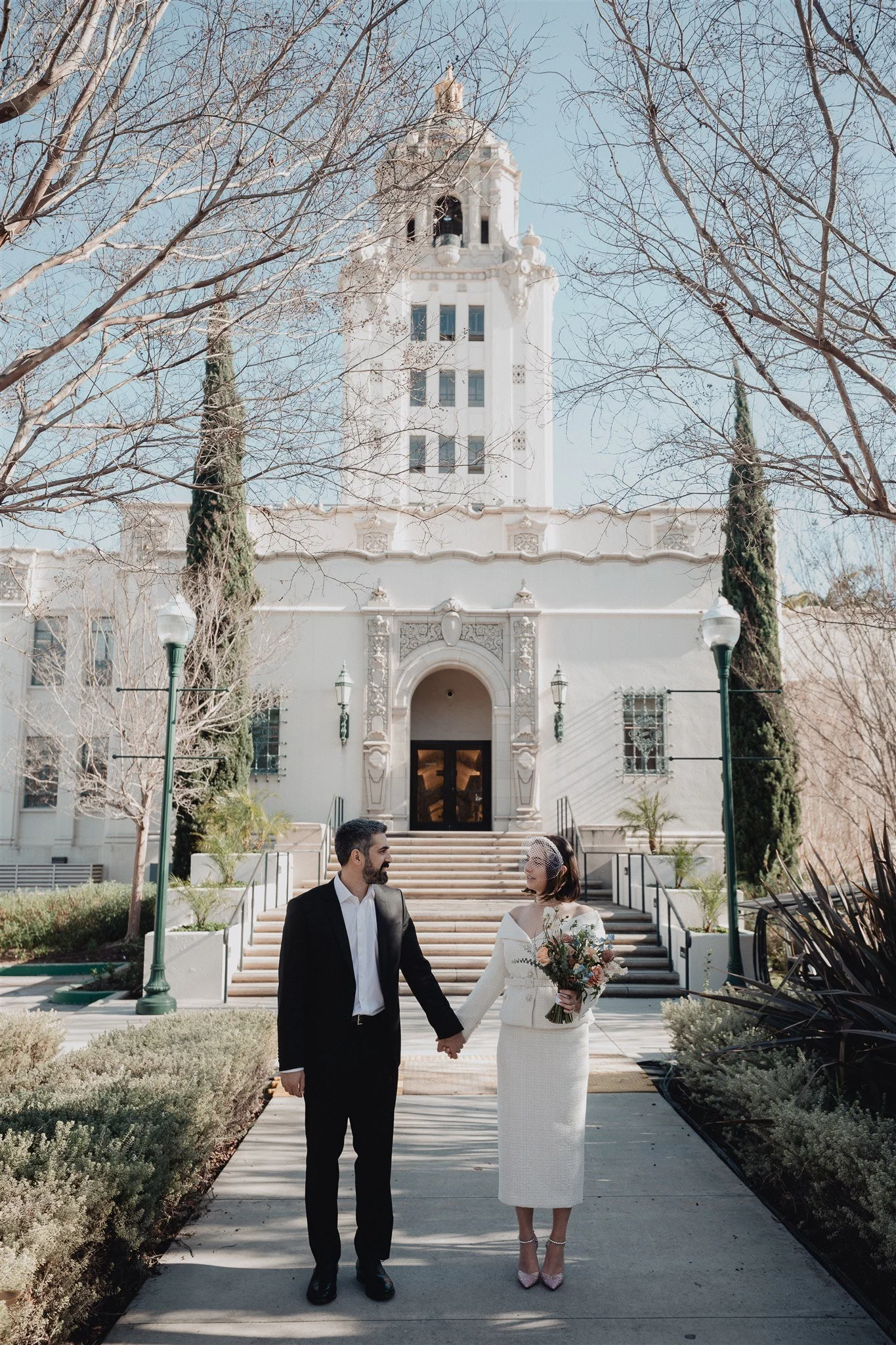 Couple walking hand in hand toward the Beverly Hills City Hall entrance after their courthouse wedding