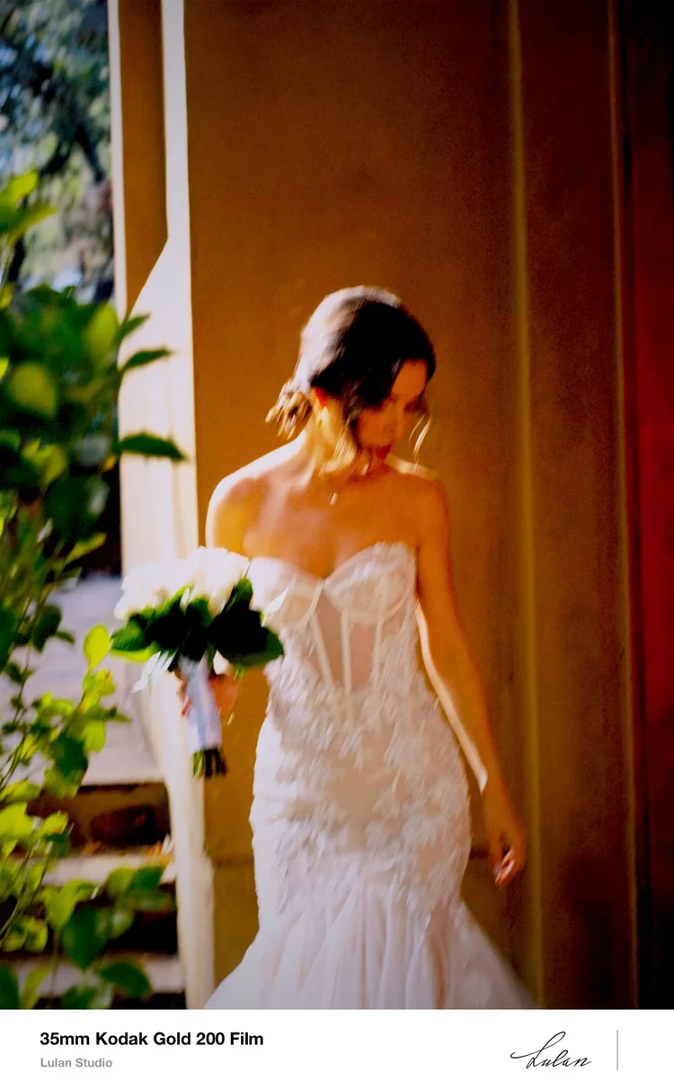Film print: bride with her bouquet in a doorway, warm light on the wall