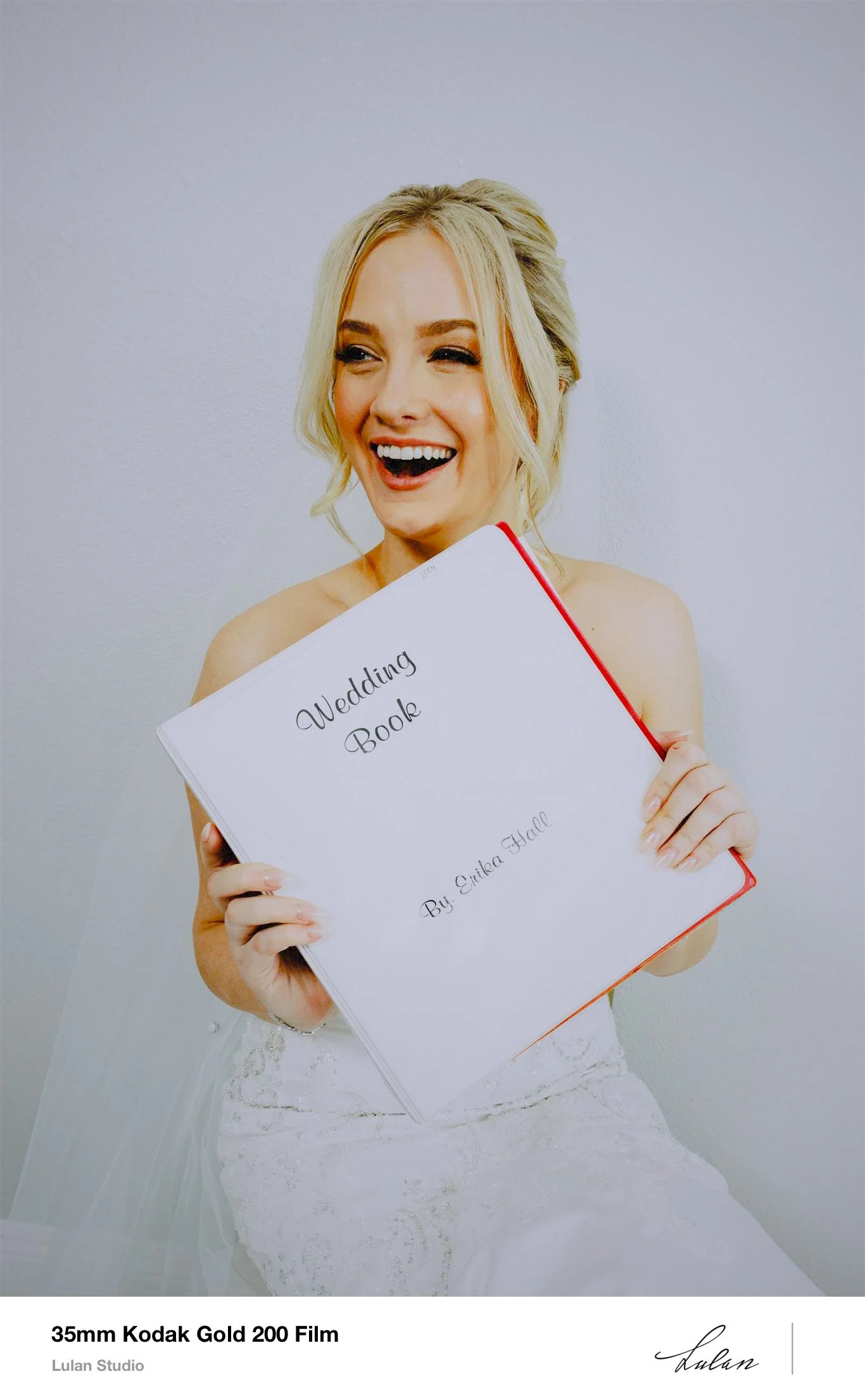 Bride laughing as she holds up a handwritten wedding book, shot on 35mm film