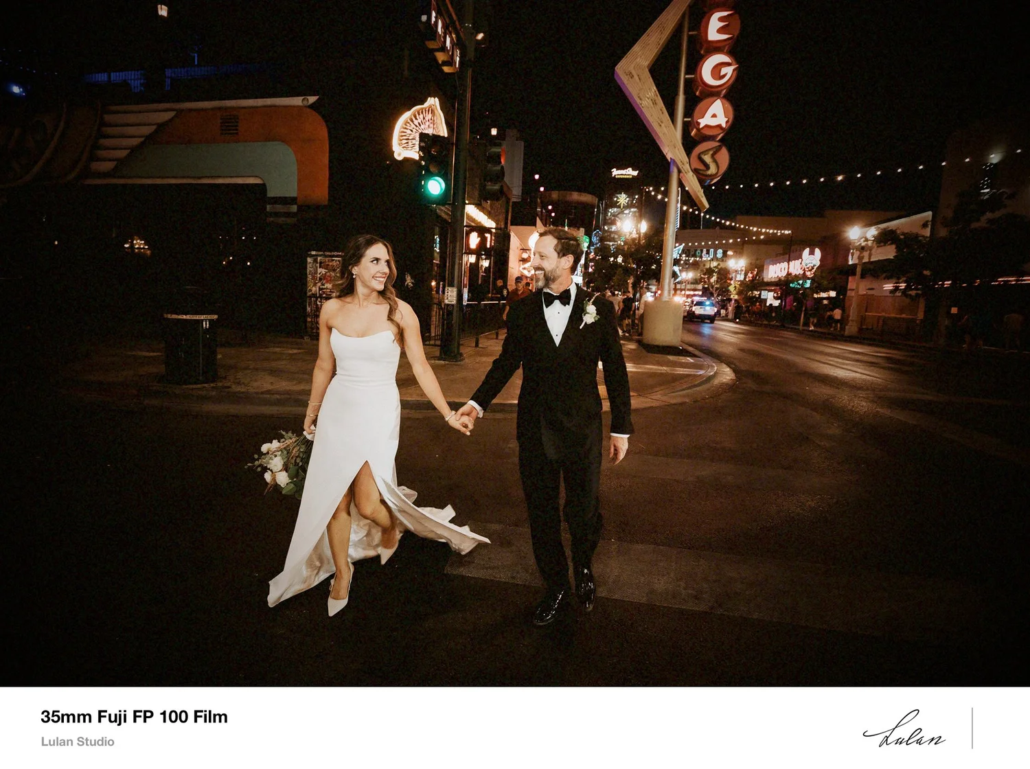 Bride and groom walking hand in hand across a neon-lit Las Vegas street at night, shot on 35mm film