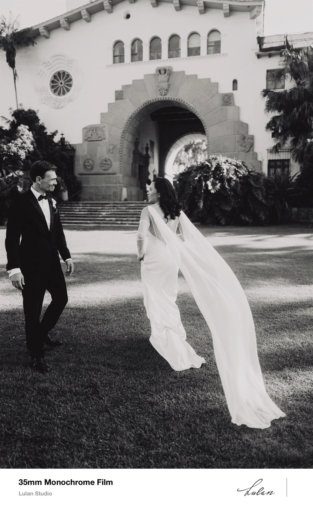 35mm black and white film — bride’s train sweeping across the lawn as her groom walks beside her