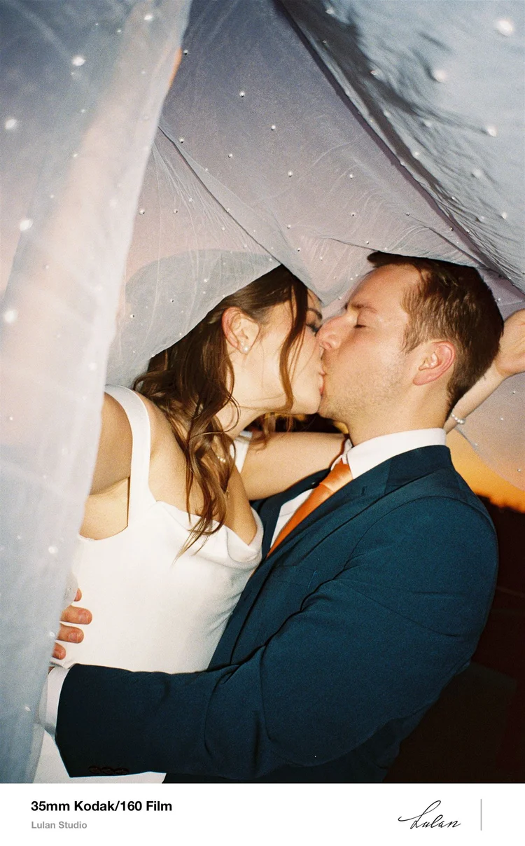 35mm Kodak 160 film — bride and groom kissing beneath a veil in soft daylight