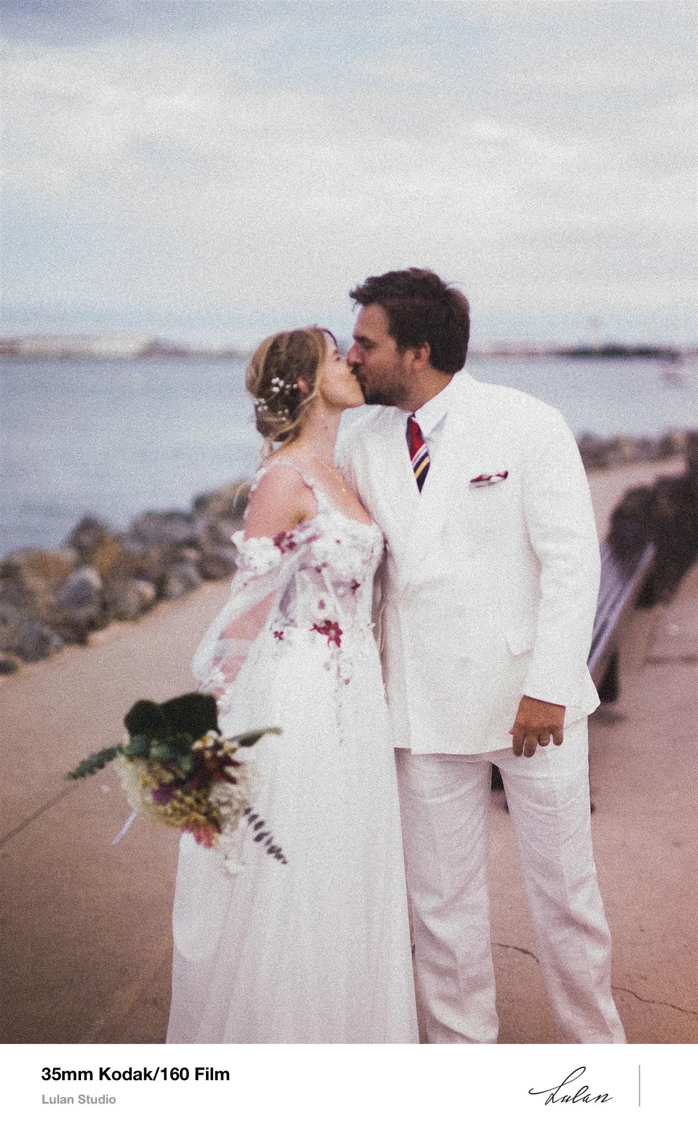 35mm Kodak 160 film frame — bride and groom kissing beside the bay