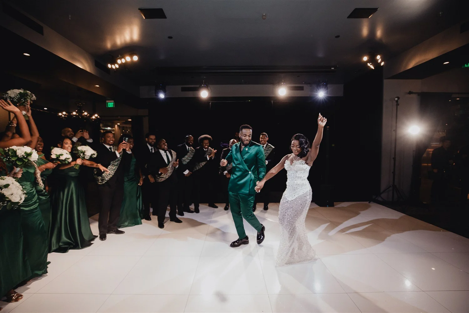 Groom in a green suit and bride dancing into their reception as the wedding party cheers