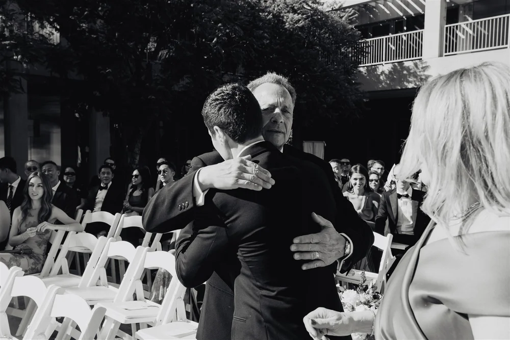 A groom walking down the aisle between both of his parents at a Los Angeles Jewish wedding