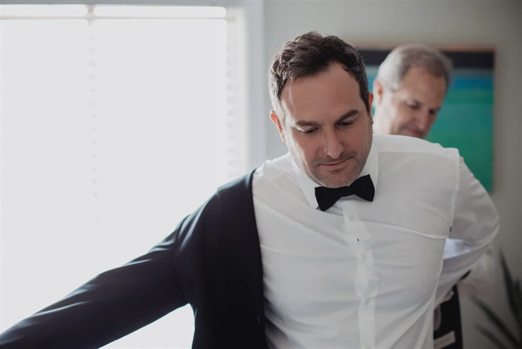 A groom being helped into his tuxedo jacket on the morning of Nicole and Danny's wedding at Castaway Burbank