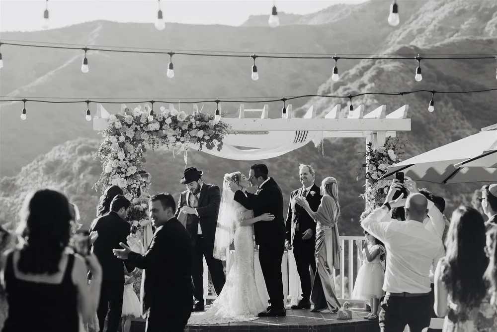 Black and white photo of a hillside wedding ceremony under cafe string lights