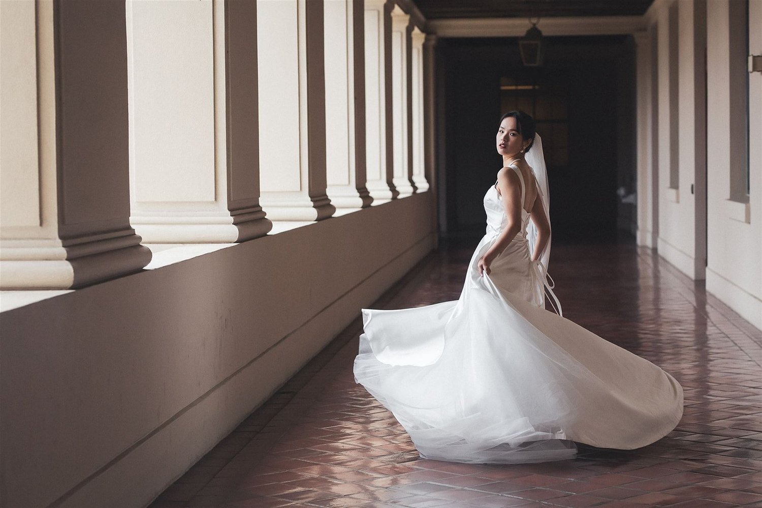 A bride turning in the colonnade at Pasadena City Hall, her veil trailing across the tiled floor