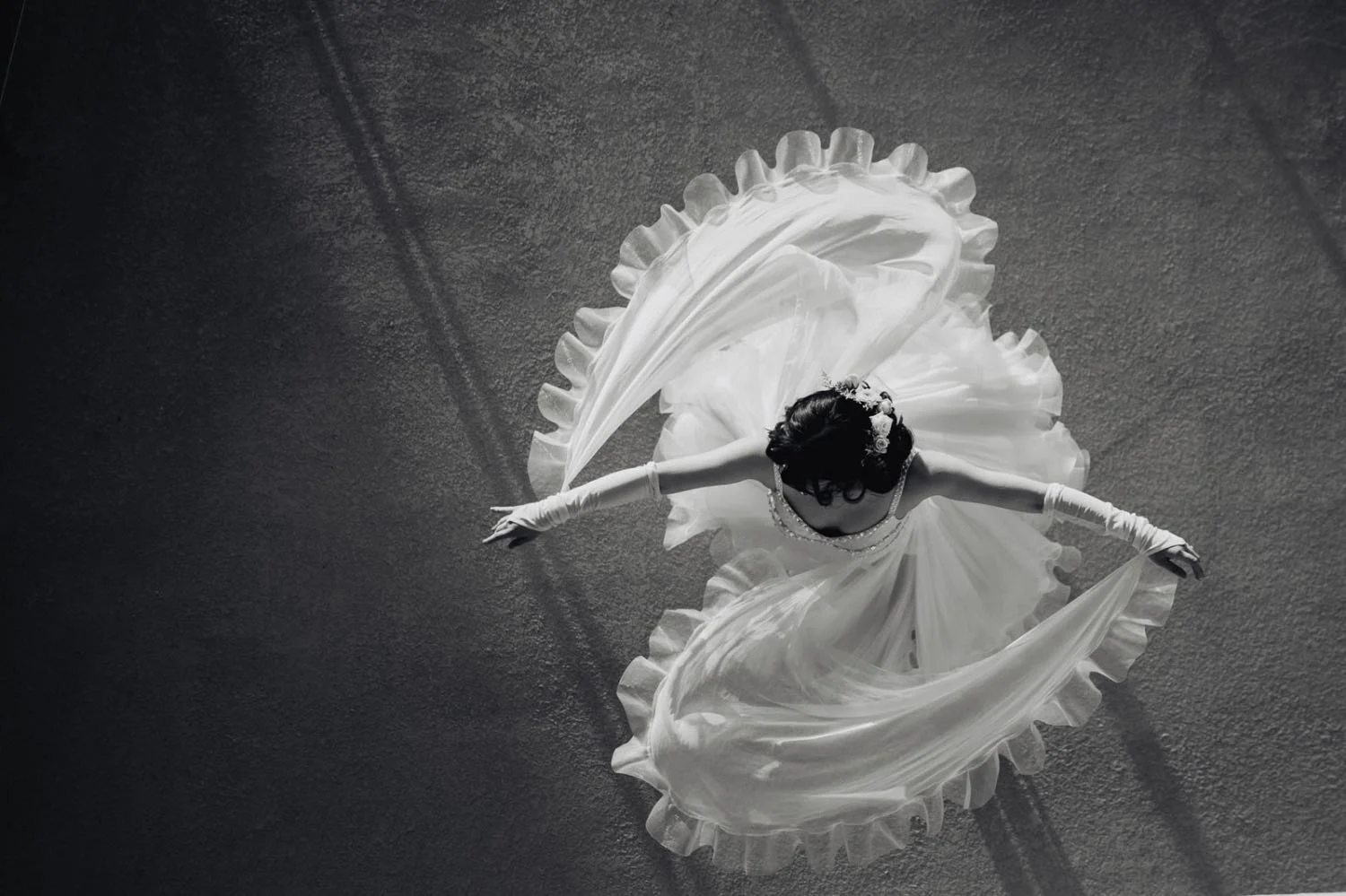 A bride in a full ballgown photographed from directly overhead, her veil and skirt fanned across a concrete floor in Los Angeles