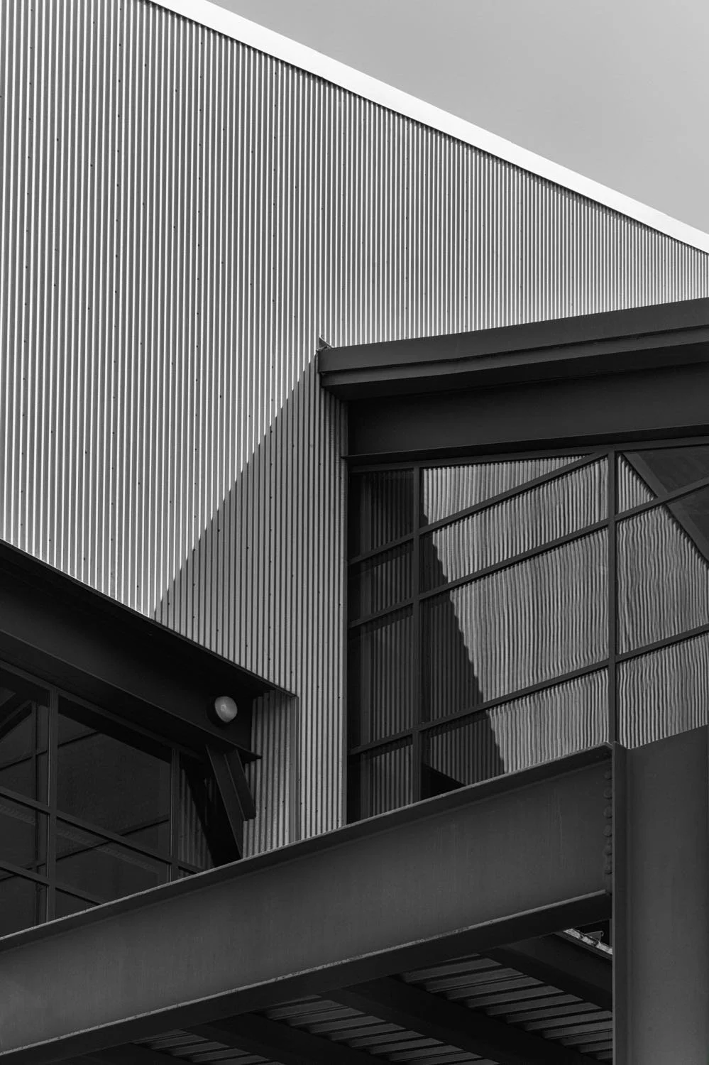 Close-up black and white photo of modern building with corrugated metal walls, large glass windows, and a metal balcony.