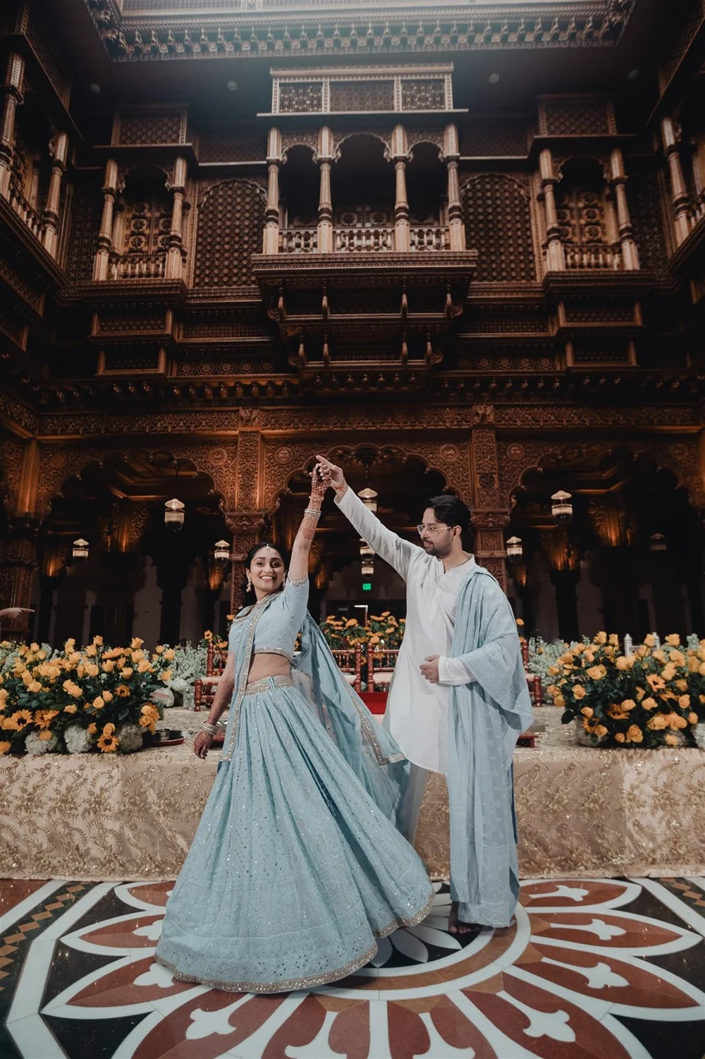 Couple in traditional Indian attire dancing in a decorated hall