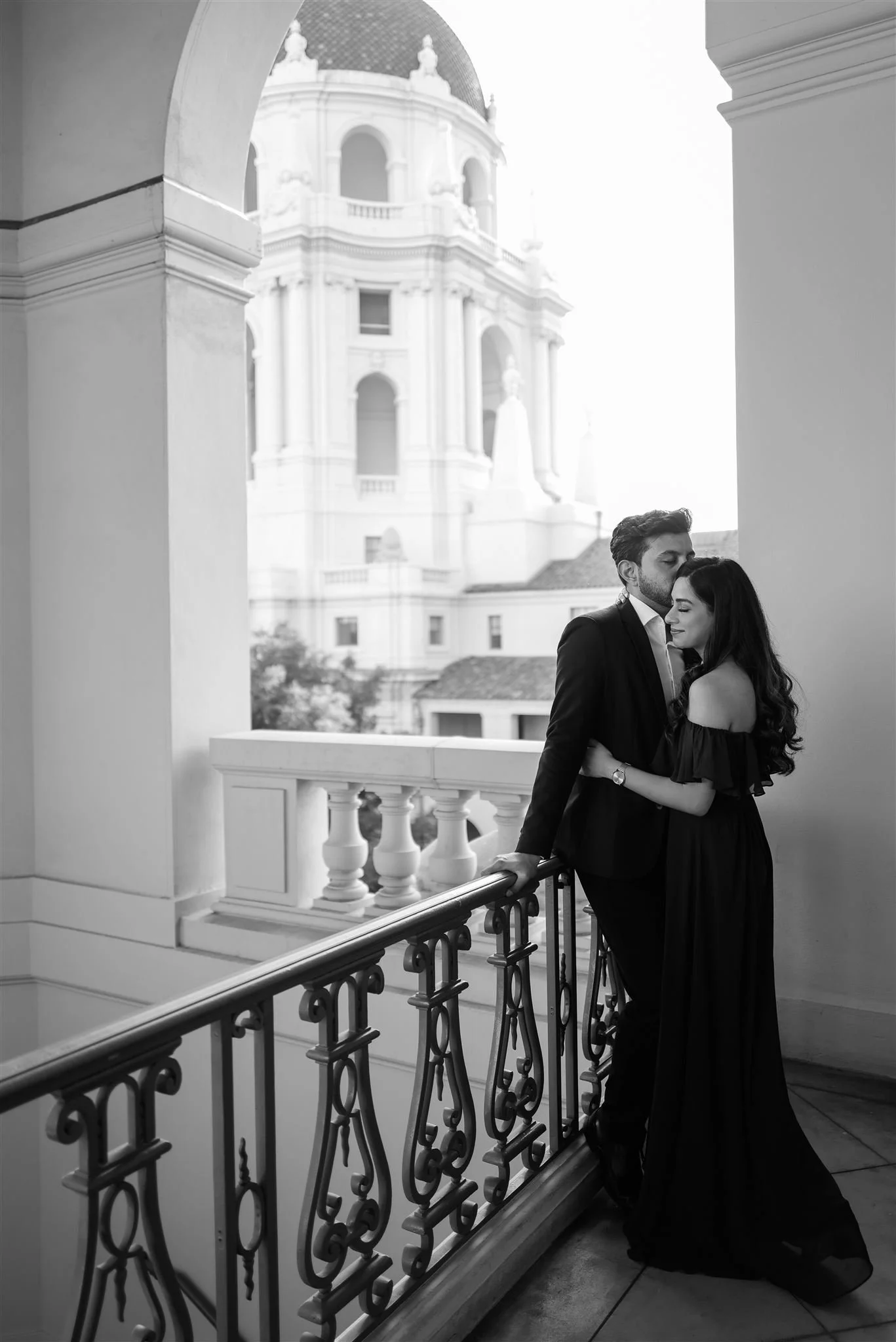 A couple on a balcony in black and white with the Pasadena City Hall dome behind them