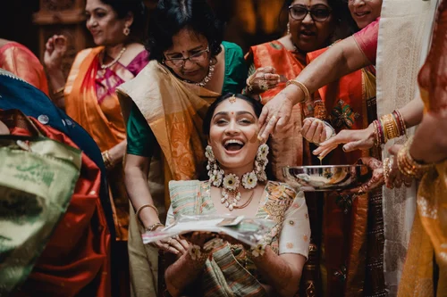Bride laughing as haldi is applied to her face