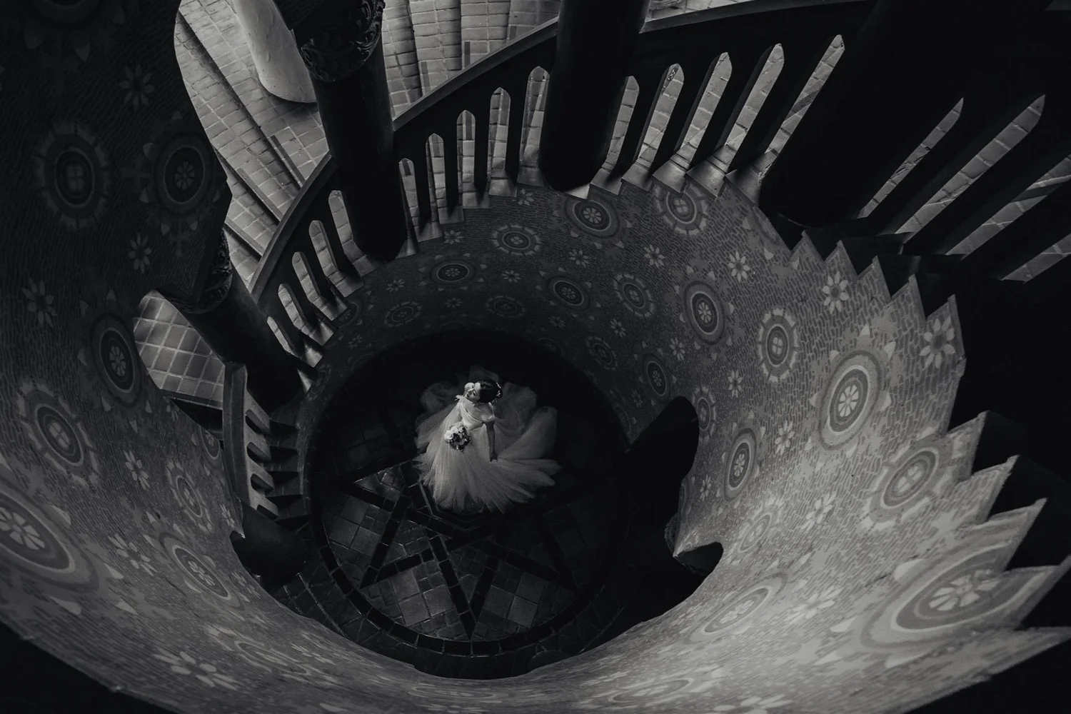 A couple seen from above at the foot of a spiral staircase, in black and white