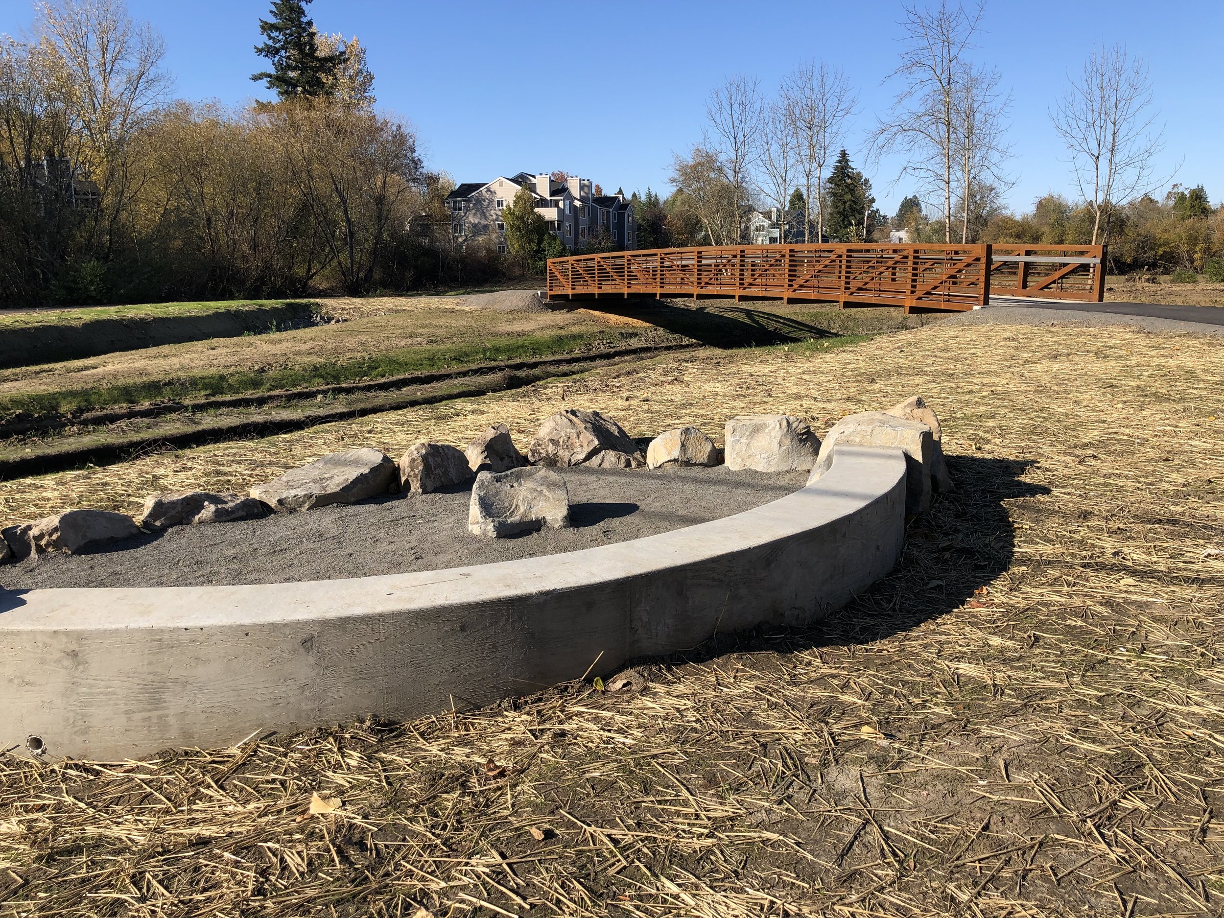 Bridge crosses fanno creek with cement and rock ringed overlook in foreground
