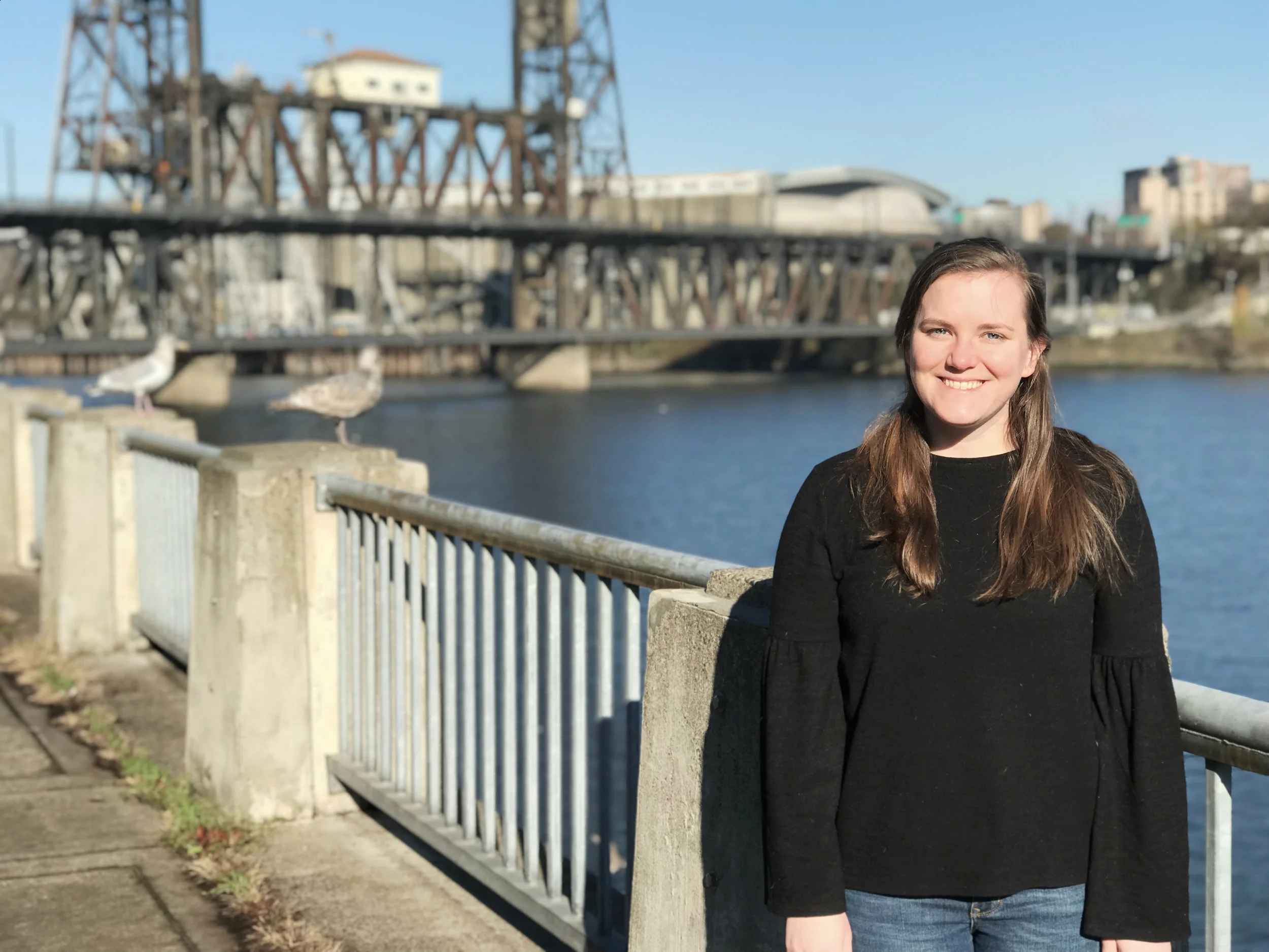 Katie Schneider stands in front of the willamette river and the steel Bridge in portland