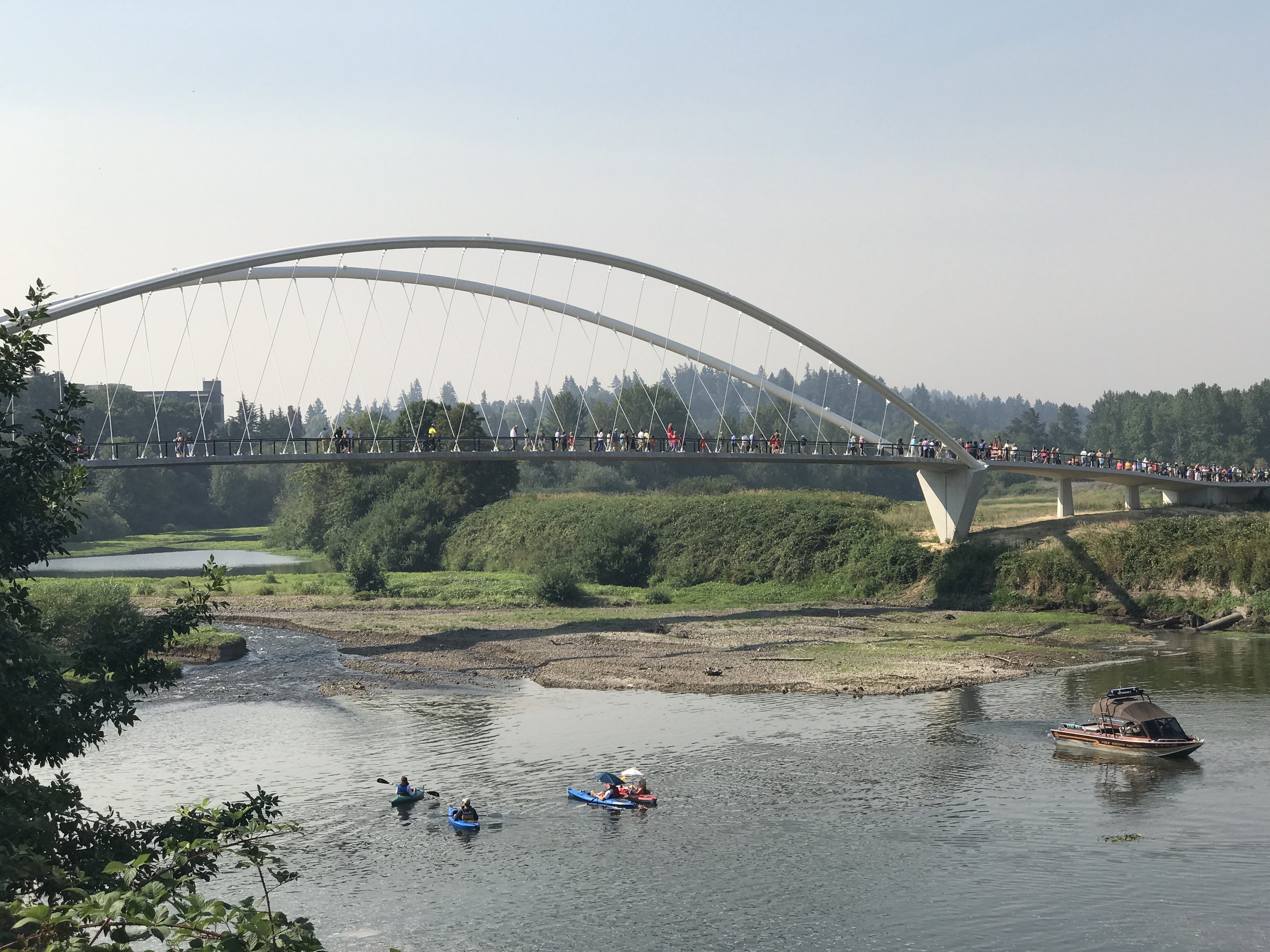 large crowds gathered at a grand opening, kayaks in river, people on suspension bridge 