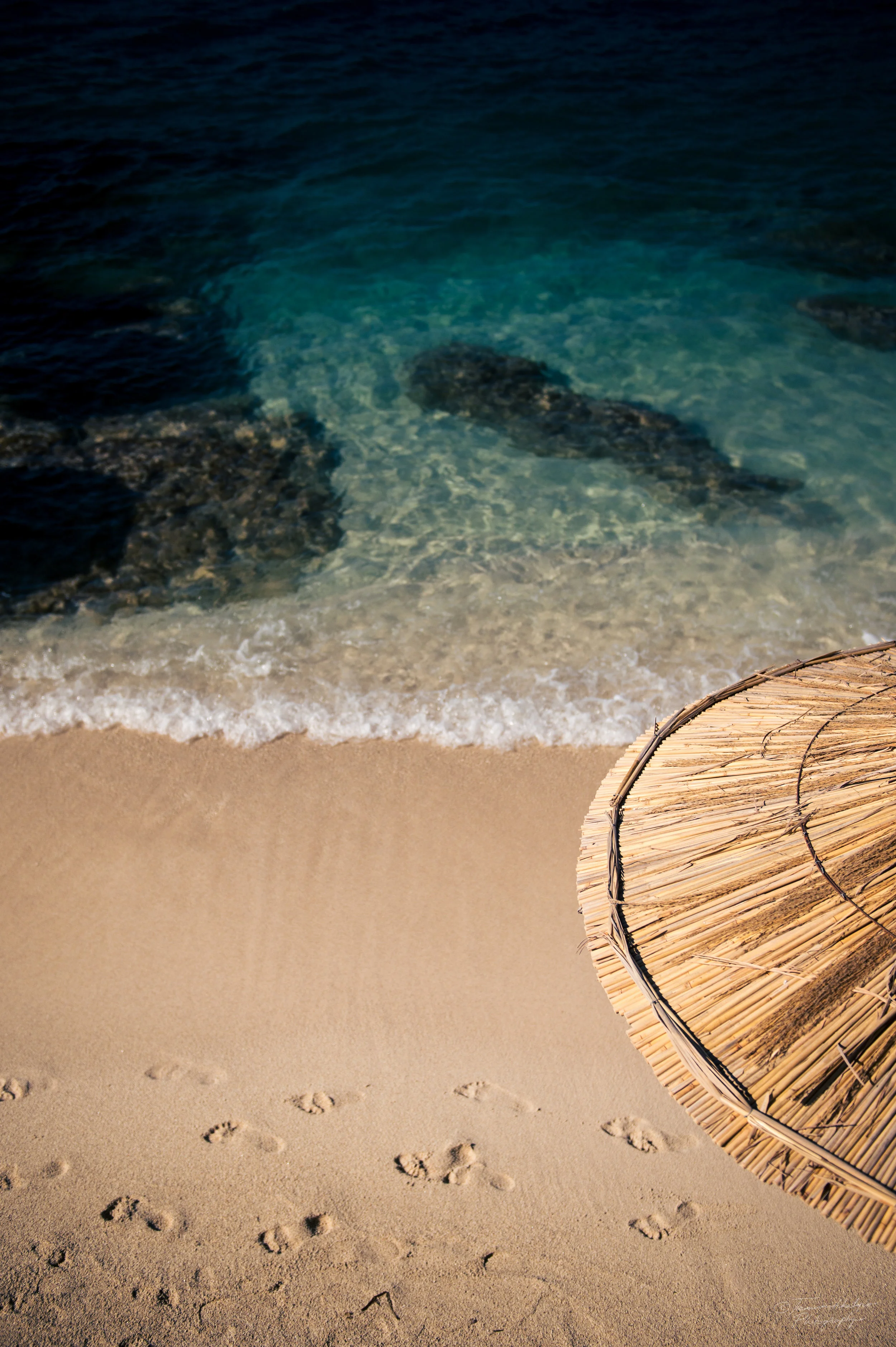 Footprints in the sand and a parasol on a beach.jpg