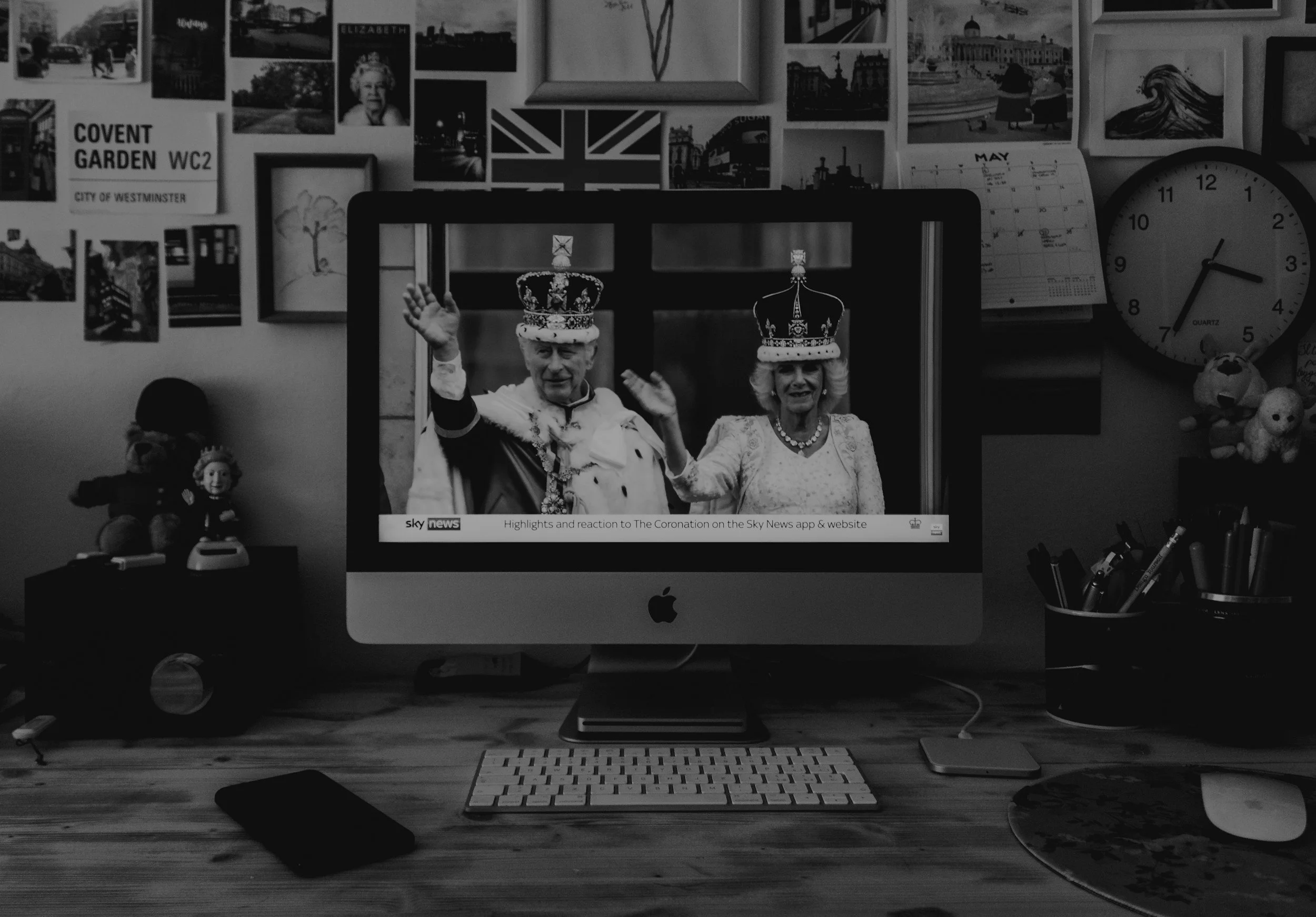 Apple computer monitor showing sky news footage of King Charles and Queen Camilla coronation, on a desk, black and white