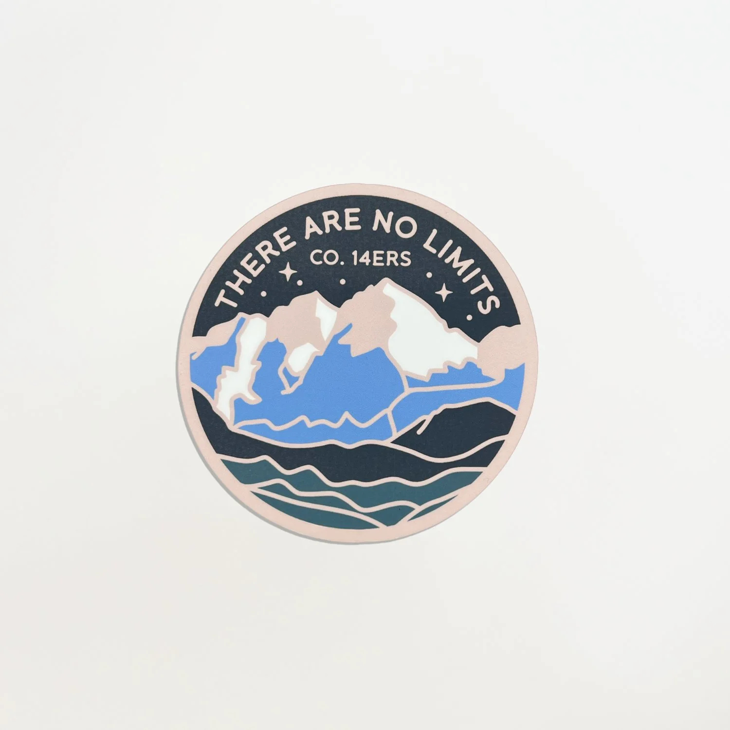 Round handmade 3-inch mountain fridge magnet with illustrated snow-capped peaks and layered blue landscape on a white background.