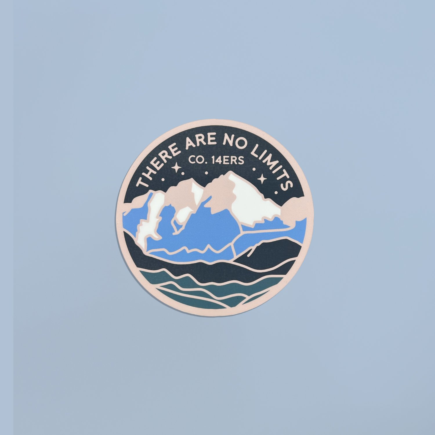 Round handmade 3-inch mountain fridge magnet with illustrated snow-capped peaks and layered blue landscape on a light blue background.