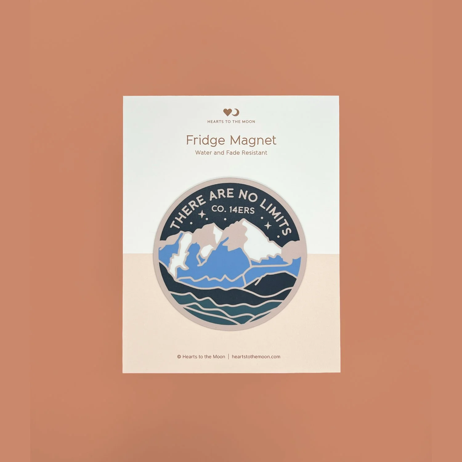 Handmade 3-inch round mountain fridge magnet displayed on its backing card against a warm copper background.