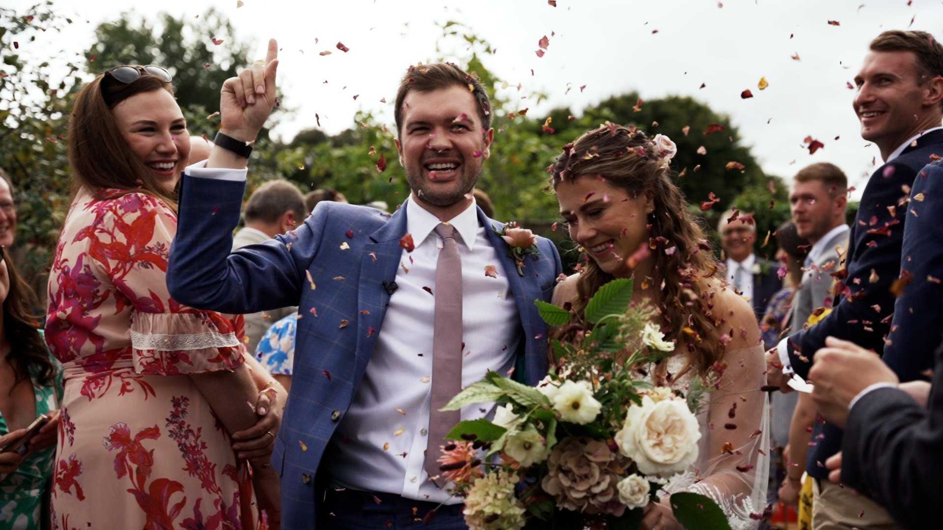 Bride and groom walking up the aisle at outdoor wedding while guests throw confetti