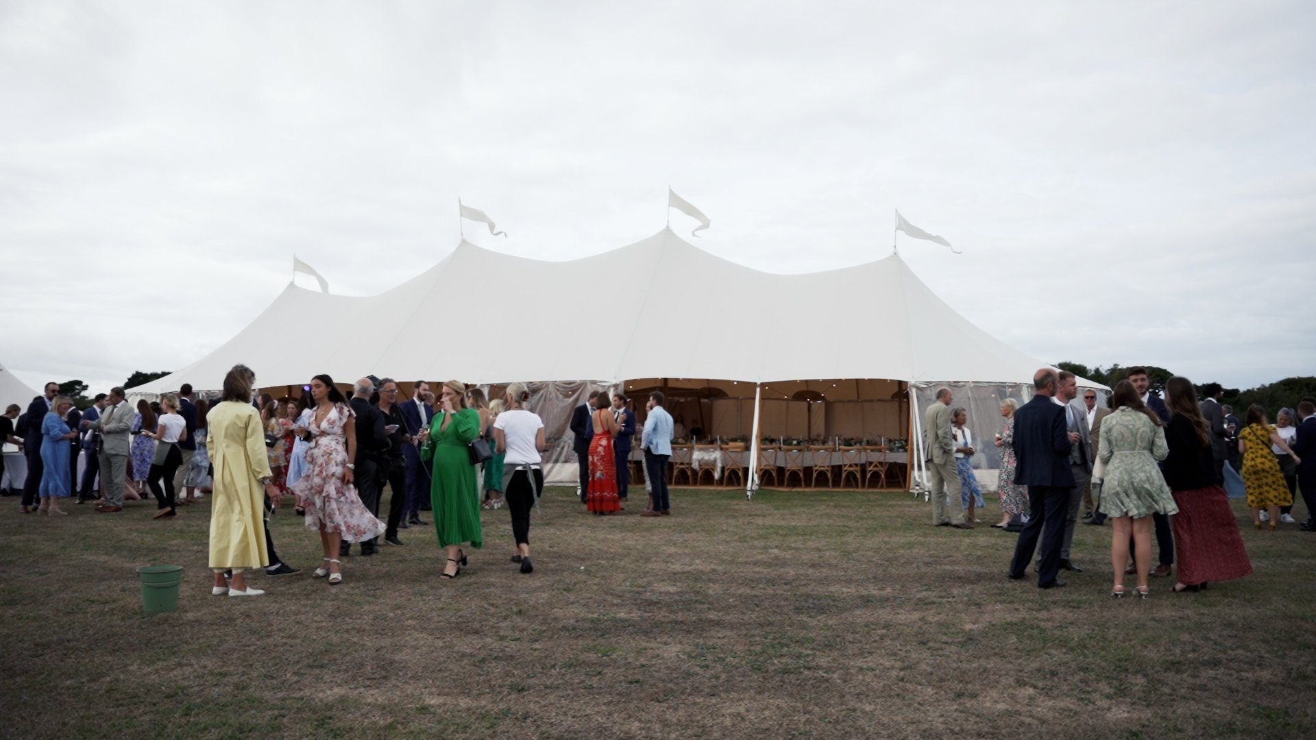 Guests chatting at outdoor wedding outside large white marquee