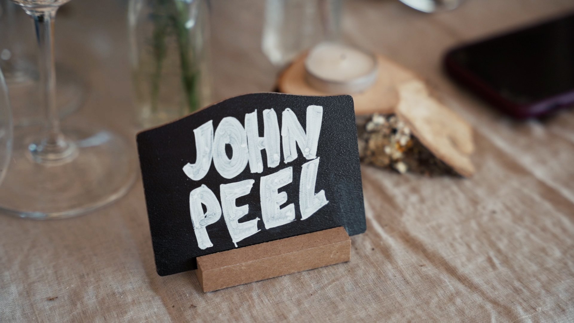 Small chalkboard sign which says 'John Peel' on table at wedding