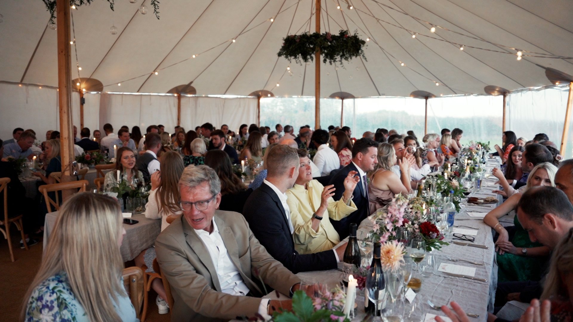 Guests sat at trestle tables inside large marquee at festival wedding