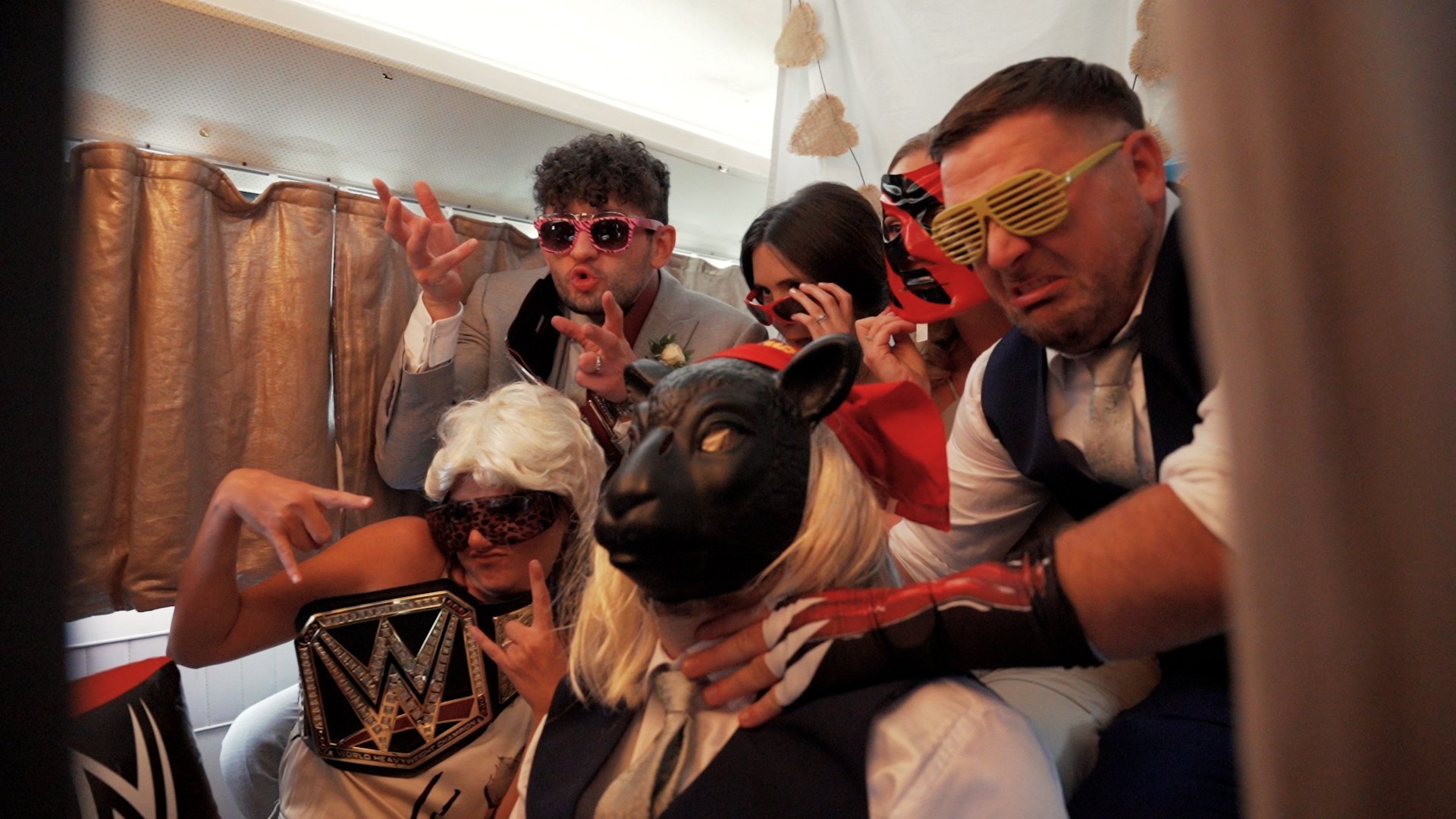 Guests at a WWE themed wedding inside a photobooth with wrestling themed props such as sunglasses, masks and WWE themed belts