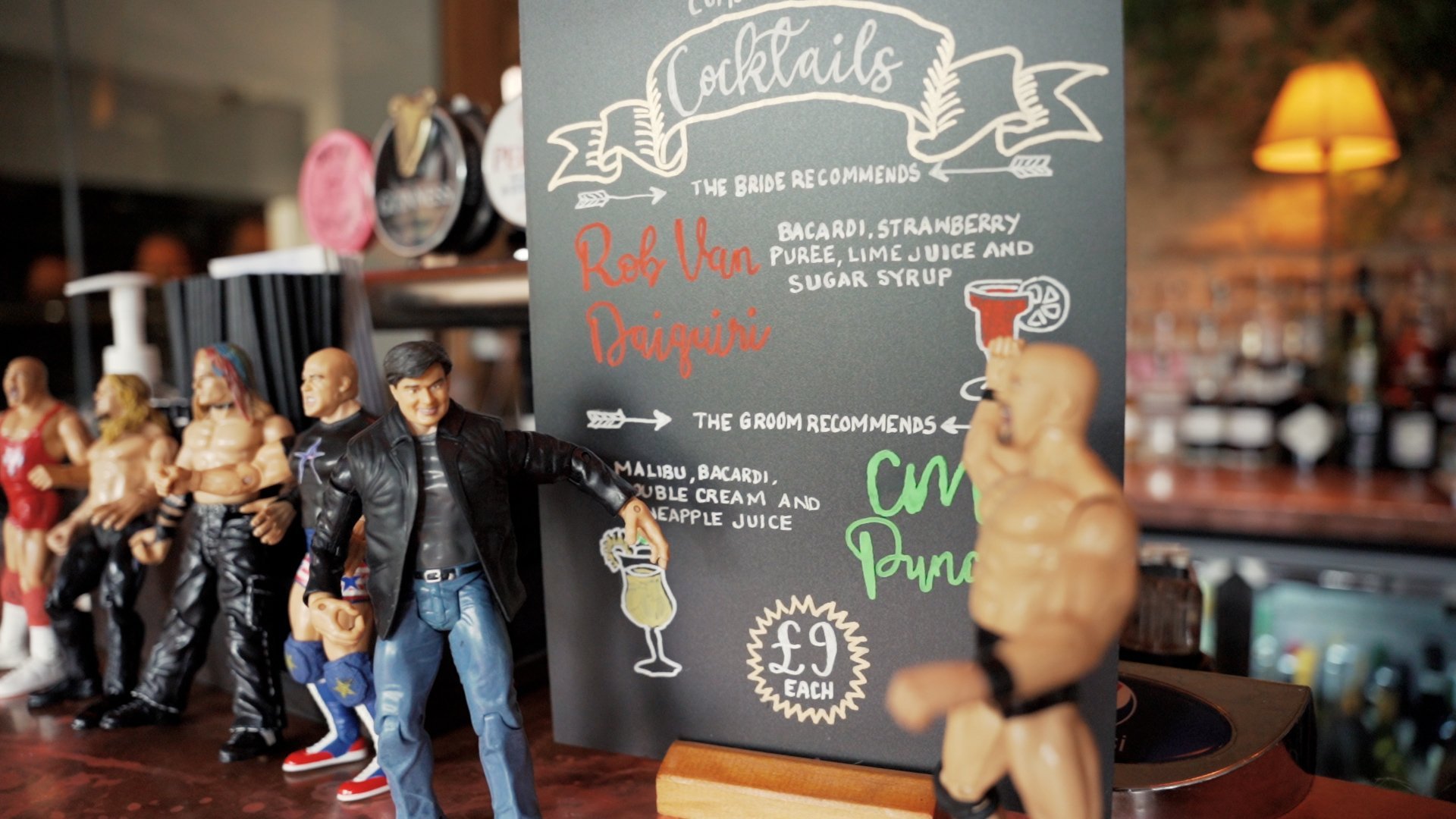 Cocktail menu written on a small blackboard with wrestling-themed figurines positioned in front of it