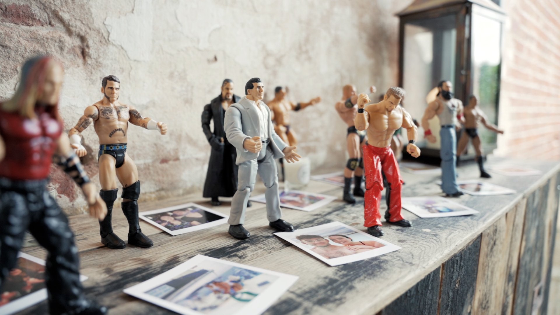 Small plastic wrestling figures of men wearing wrestling outfits on table surrounded by photos of a man and a woman