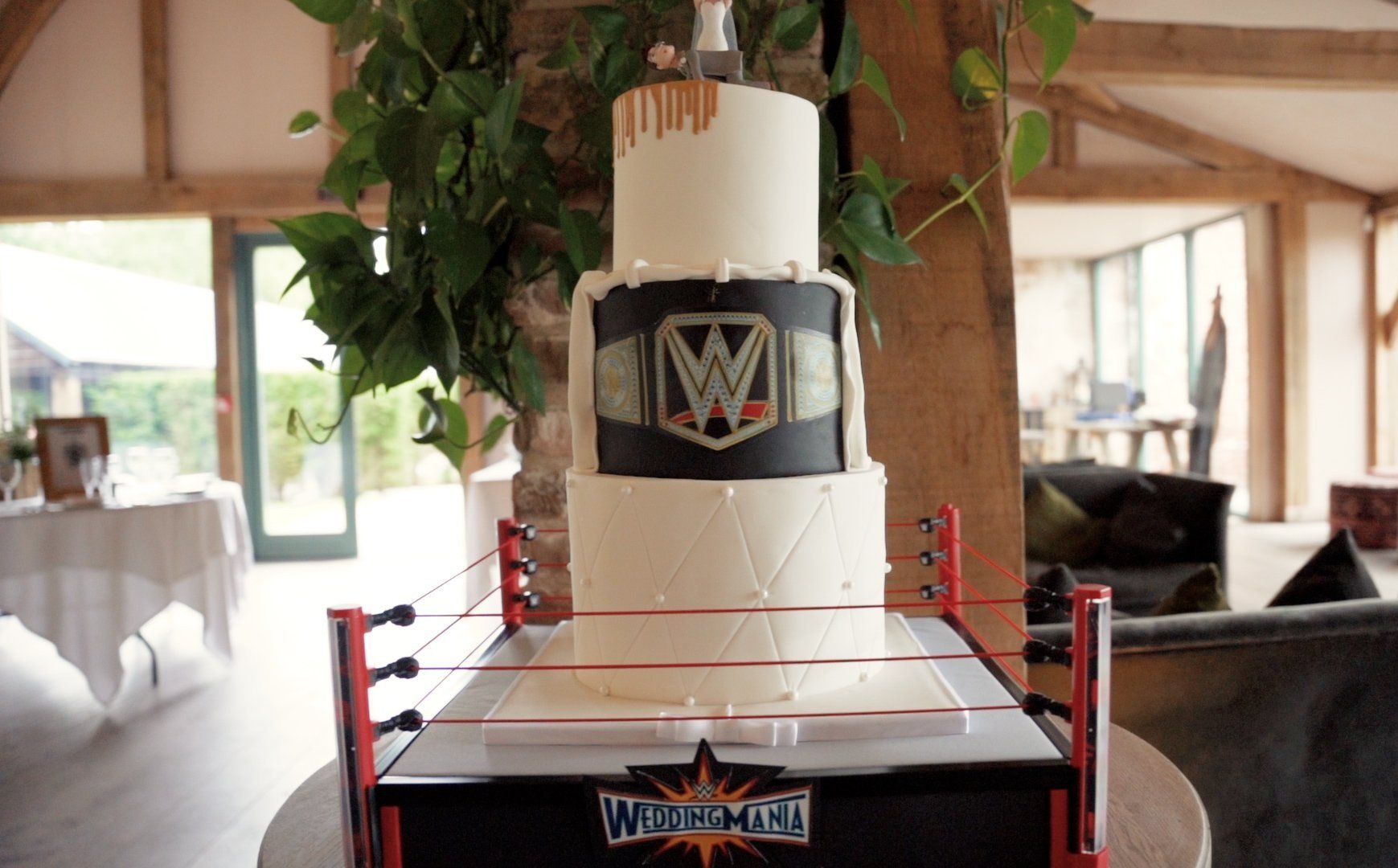 WWE wedding cake inside a mini wrestling ring. The cake is a three-tiered wedding cake with white and black icing and a WWE logo