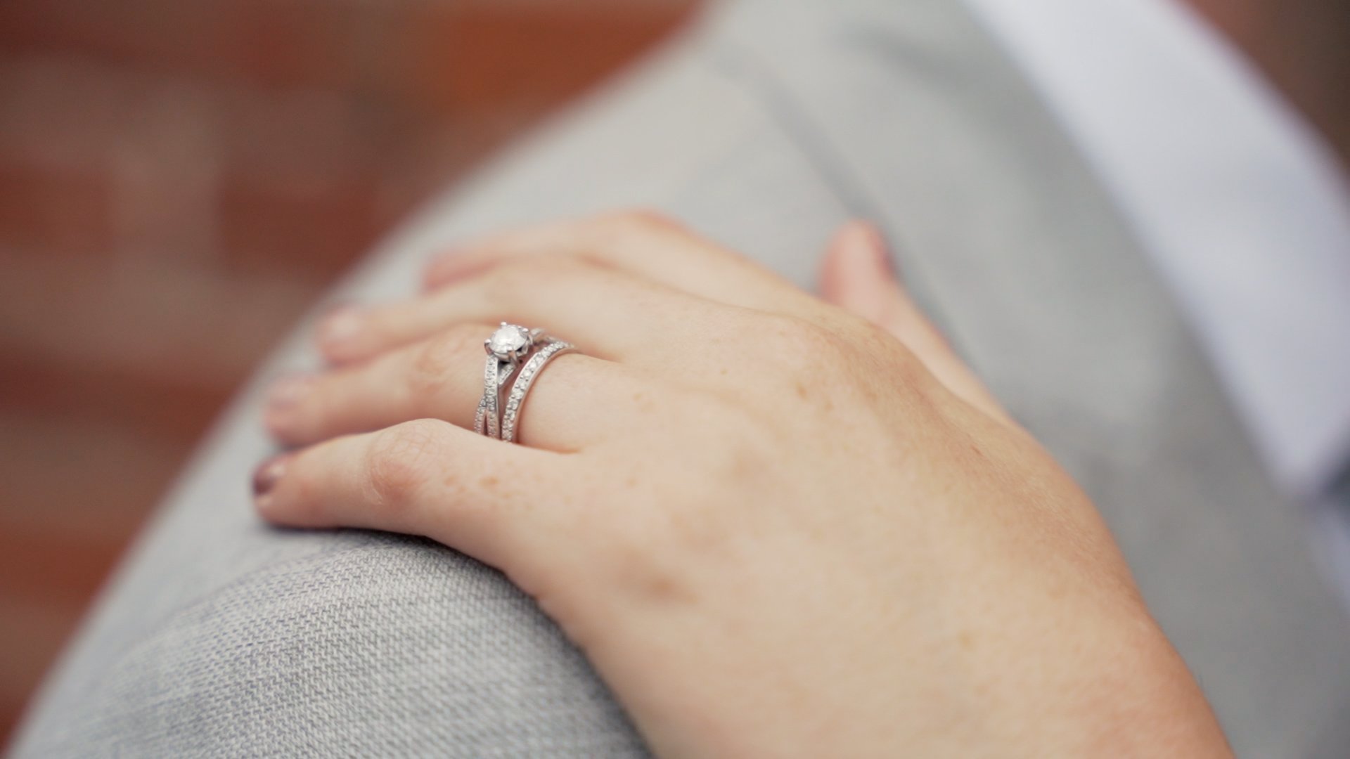 Up close photography of a bride wearing a wedding ring with her hand placed gently on her husband's shoulder