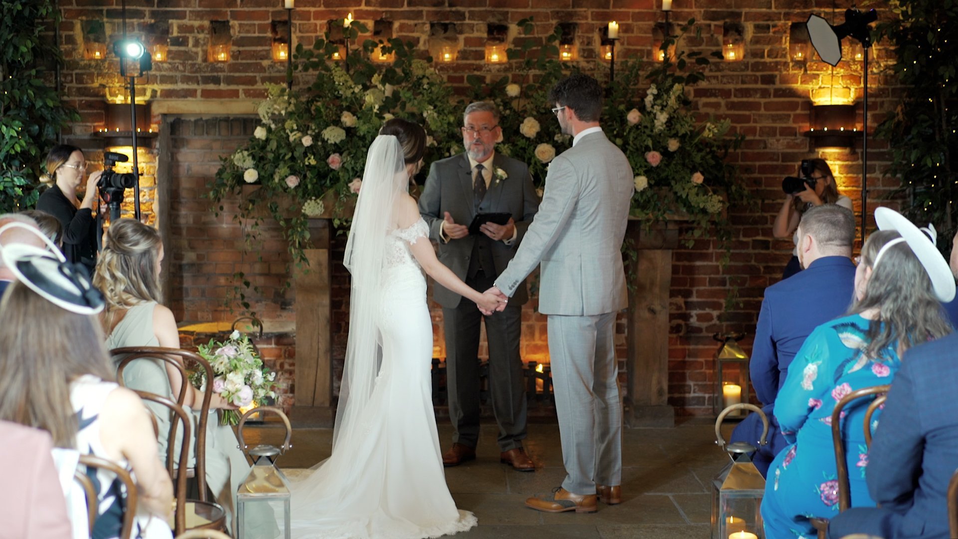 A bride and groom holding hands in front of a minister while saying their wedding vows as wedding guests look on