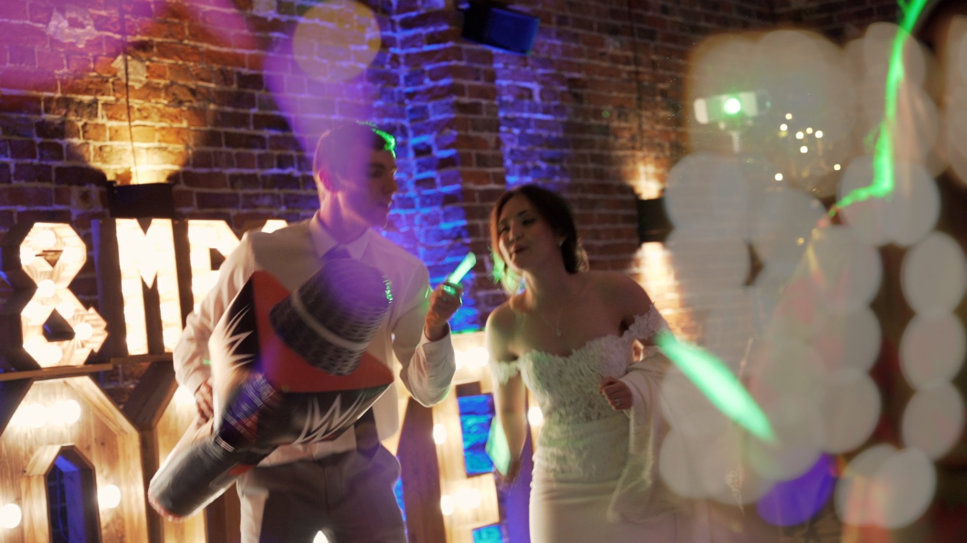 Bride and groom dancing at their wedding reception while holding large inflatable WWE wrestling props