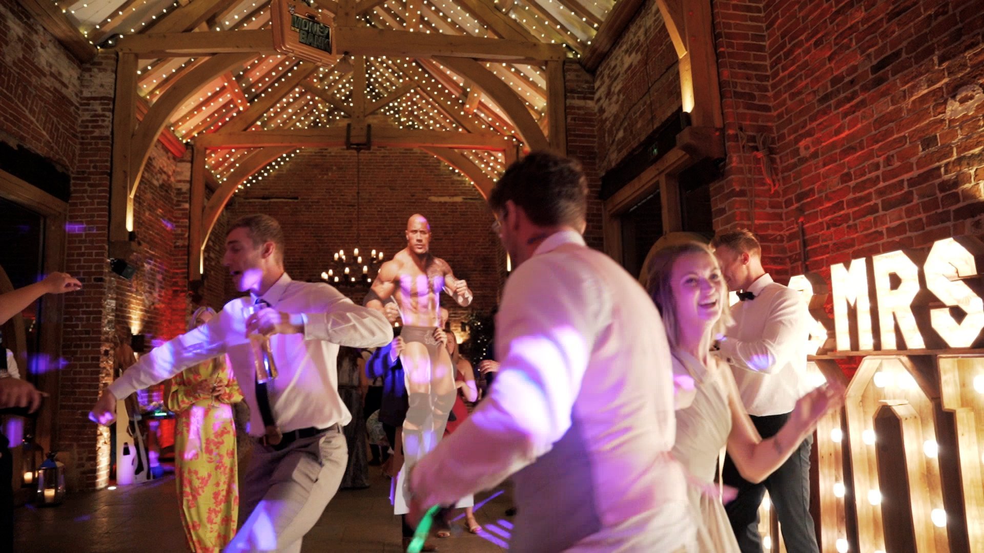 Wedding guests dancing inside a beautiful wedding venue in front of life-sized cardboard cut outs of famous wrestlers