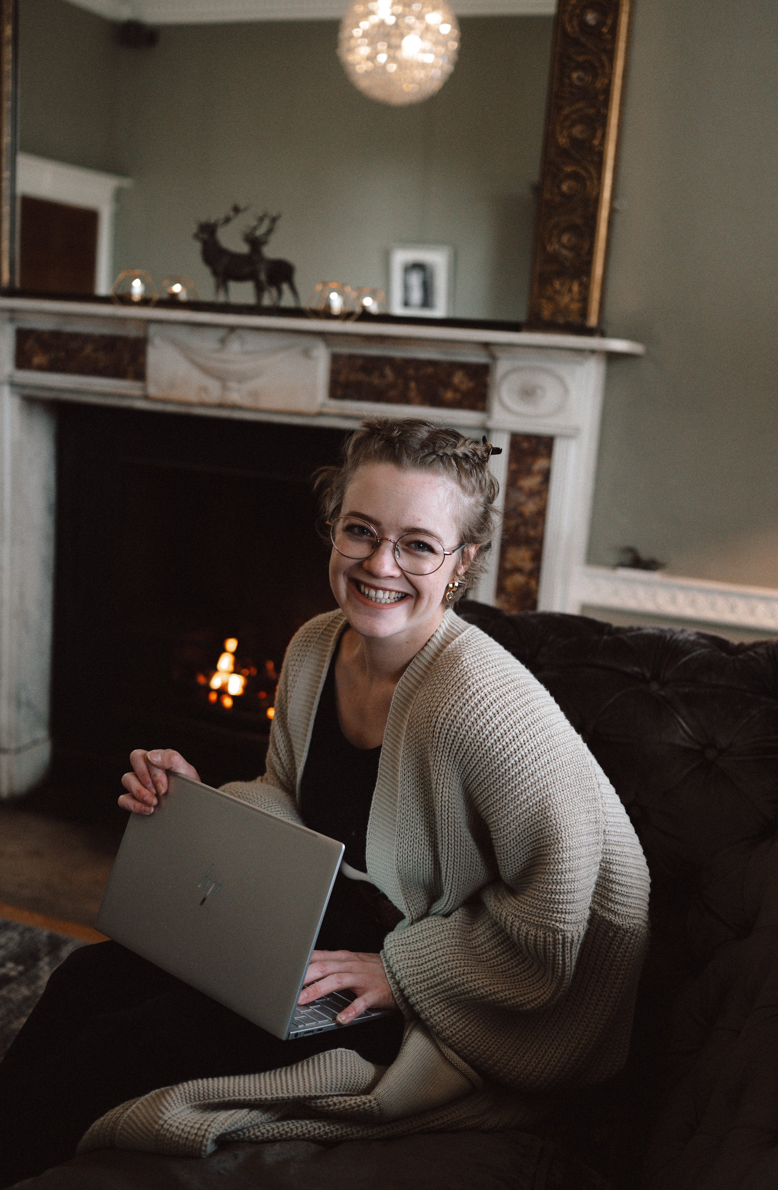 Photo of Alannah Veitch, wedding content creator. She is sitting in a cosy lounge beside a fire while working on her laptop