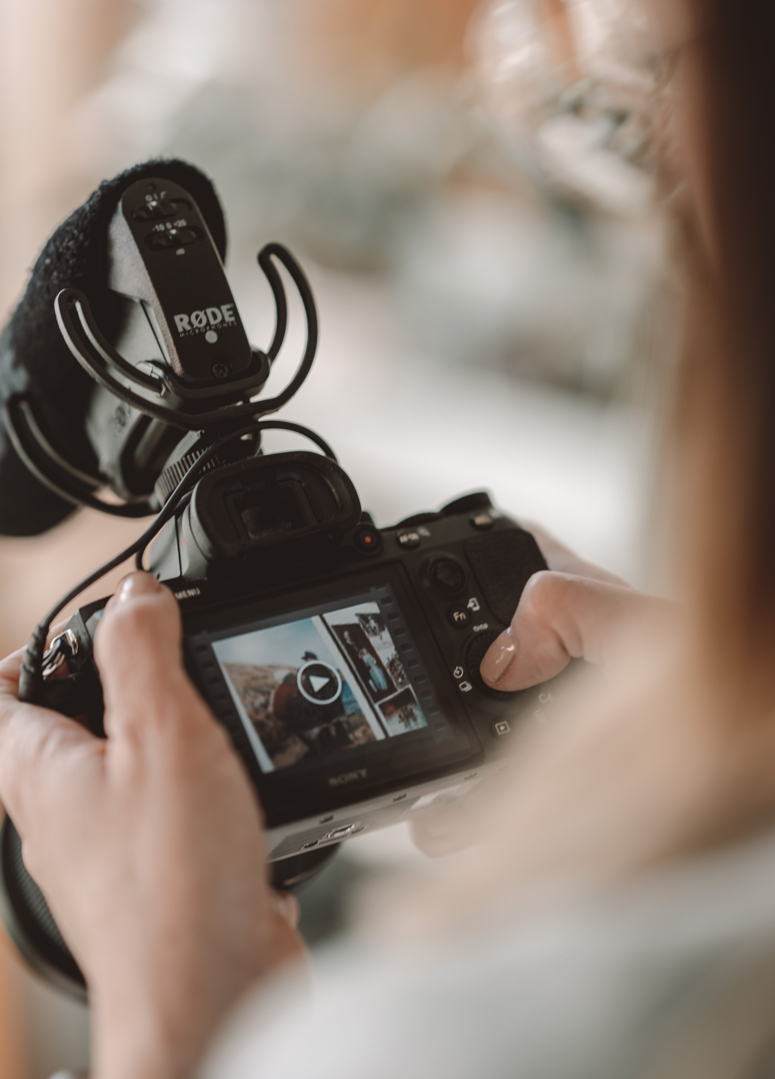 Woman's hands holding a professional video camera. The woman is pressing a button on the back of the camera.