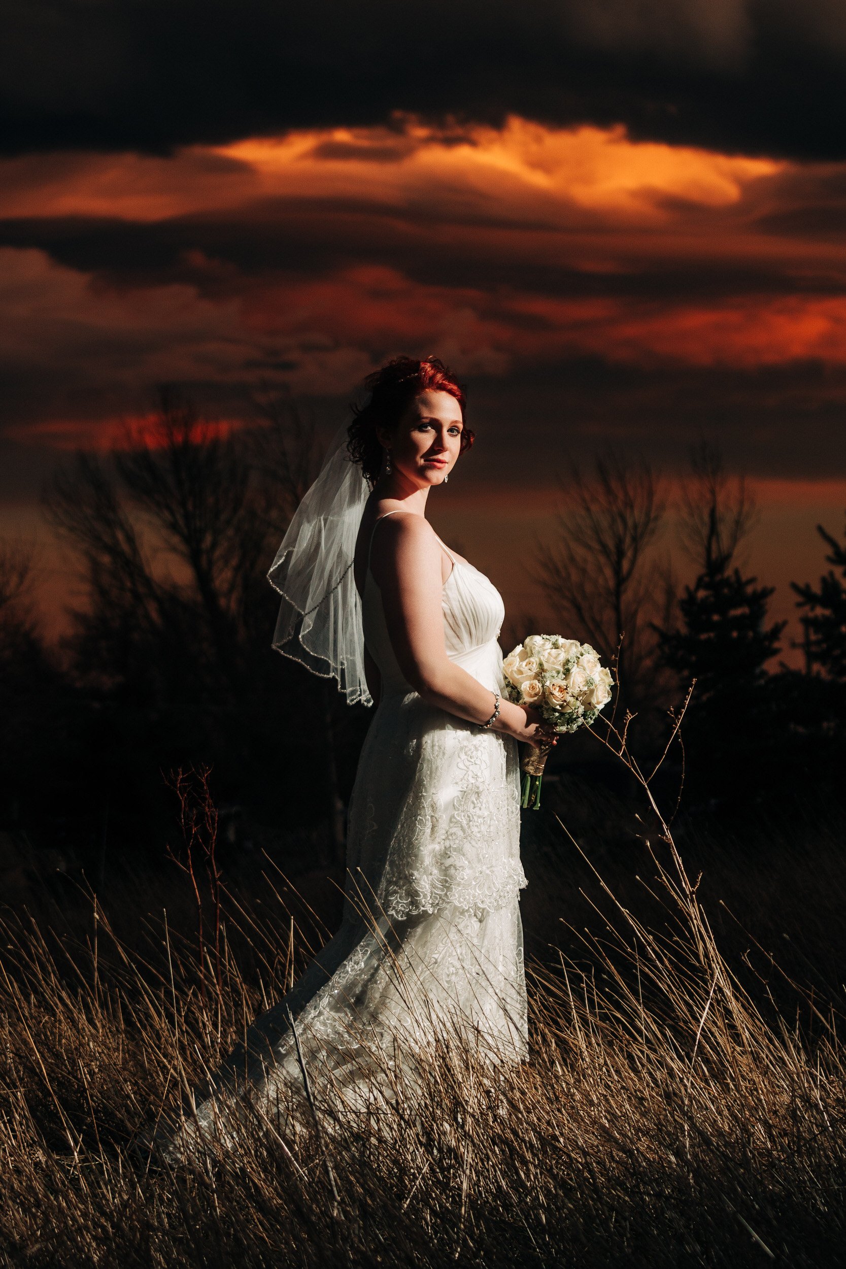 Bride poses for a portrait in front of a dramatic red and orange Winter sunset during a Greenbriar Inn wedding reception in Boulder, Colorado