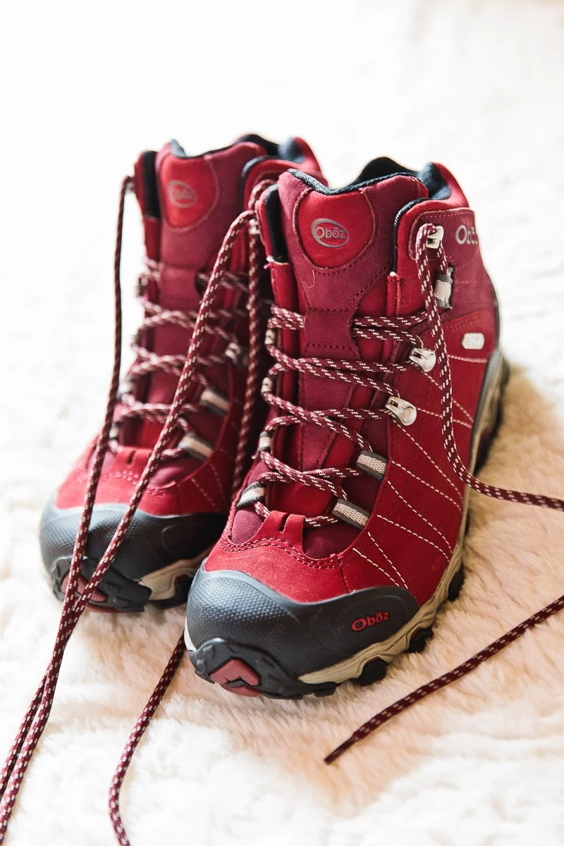 Red hiking boots with black soles and patterned laces on a fluffy white surface. The boots appear sturdy and ready for outdoor adventures.