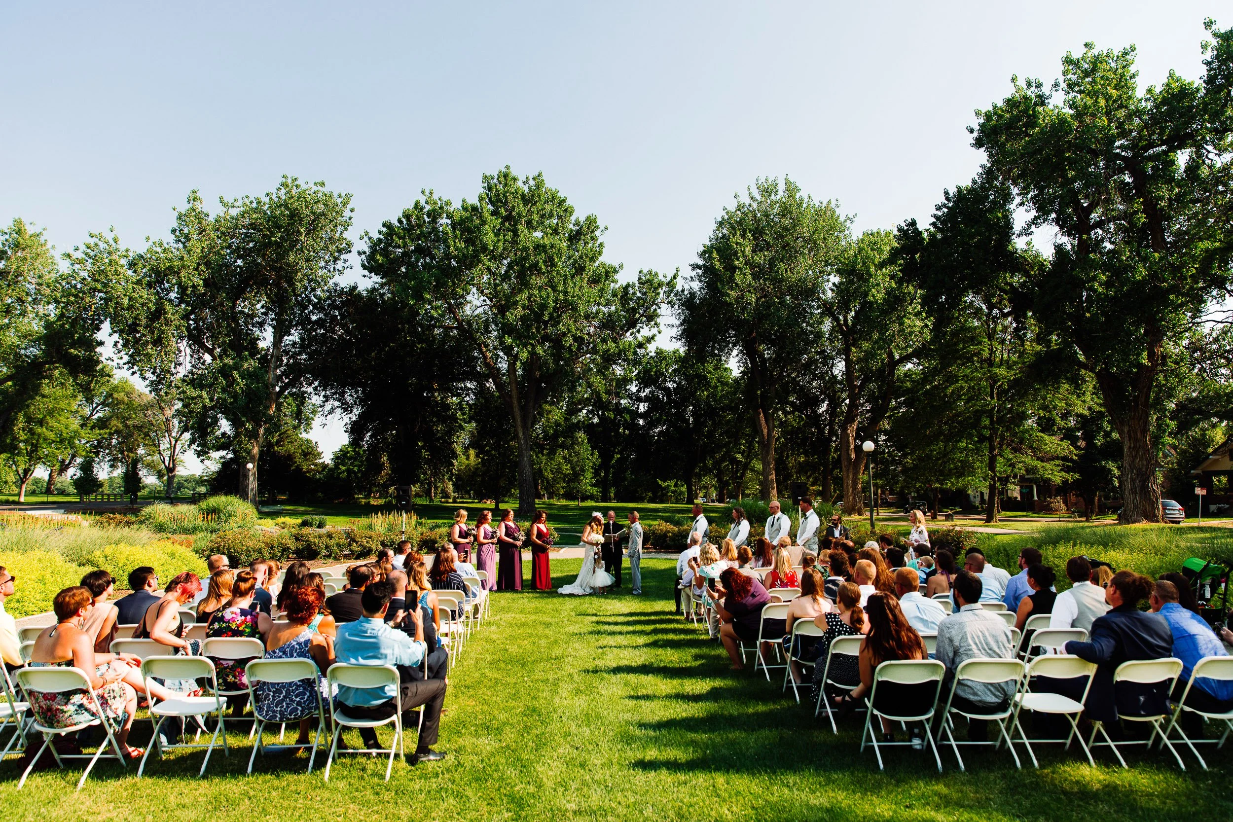 Wide scene of guests watching bride and groom exchange vows during a Washington Park Boathouse wedding in Denver, Colorado