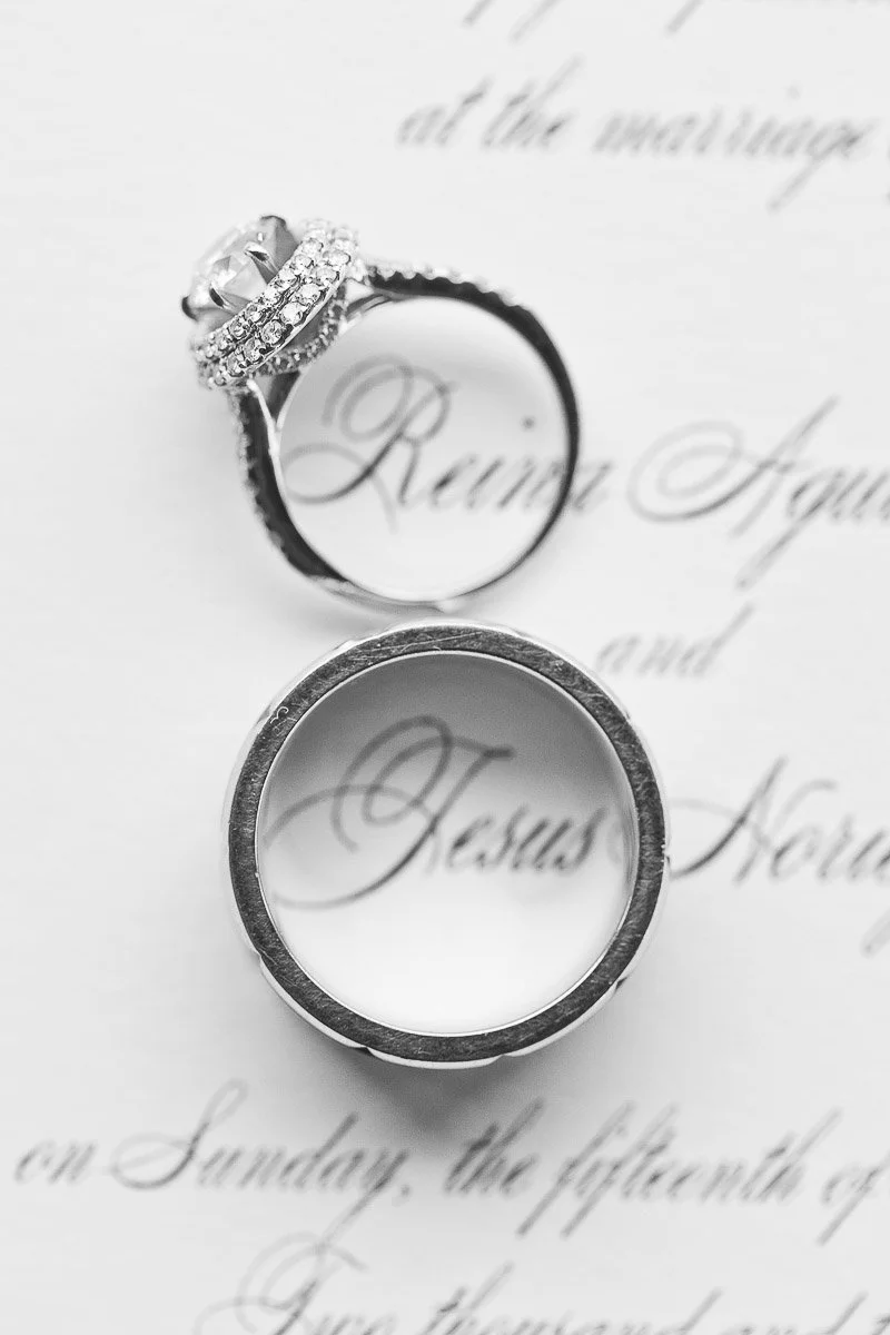 Close-up of wedding rings on an invitation. An ornate engagement ring and a simple wedding band encircle elegant script, creating a romantic tone.