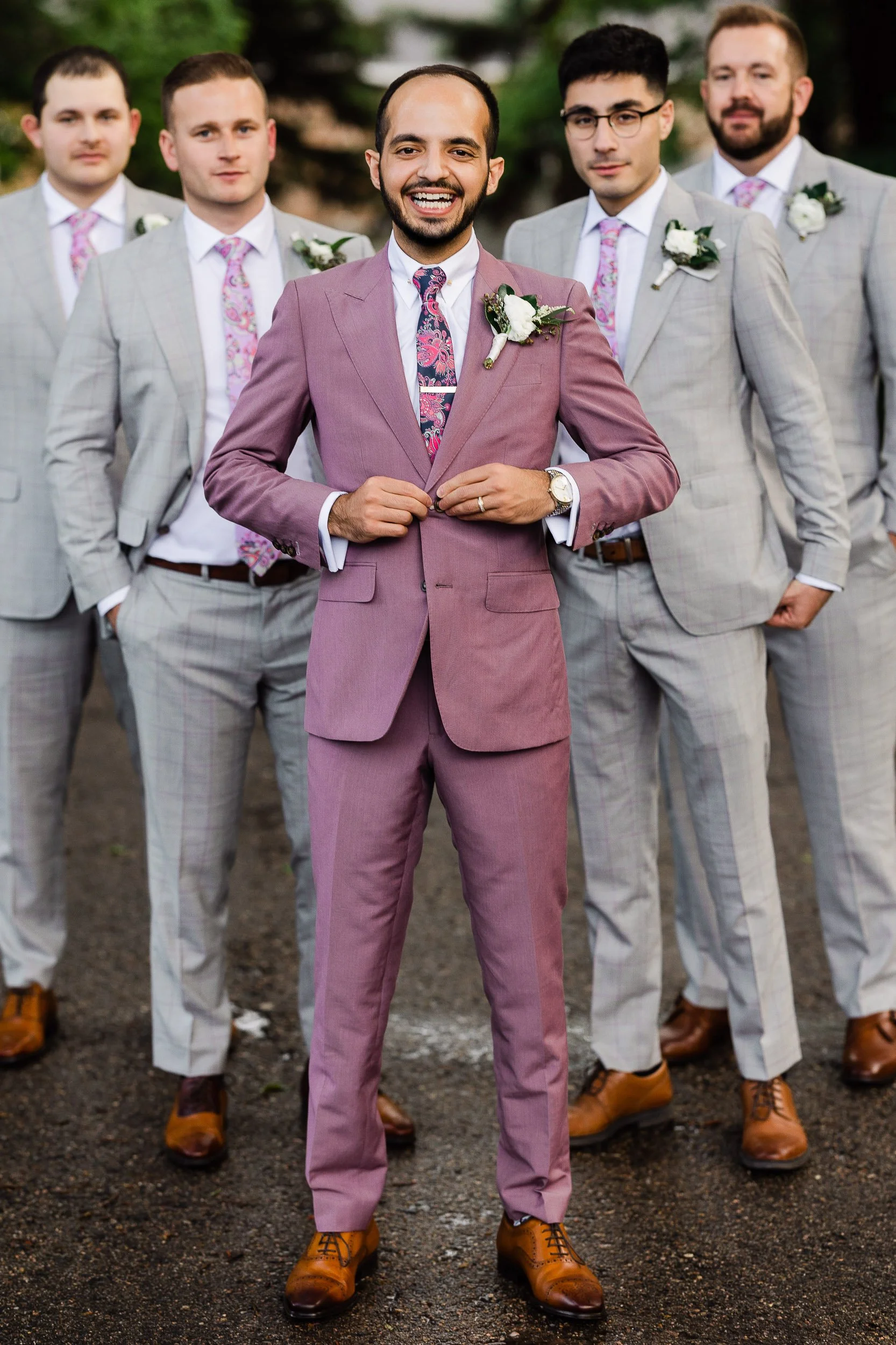 A groom formally dressed in purple stands in front of his groomsmen in grey during a Black Canyon Inn wedding in Estes Park, Colorado.