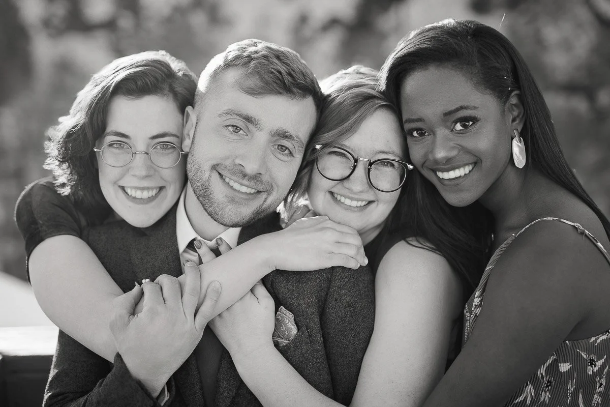 A black and white photo of four friends hugging closely, smiling warmly. The group expresses happiness and camaraderie, creating a joyful and intimate atmosphere.