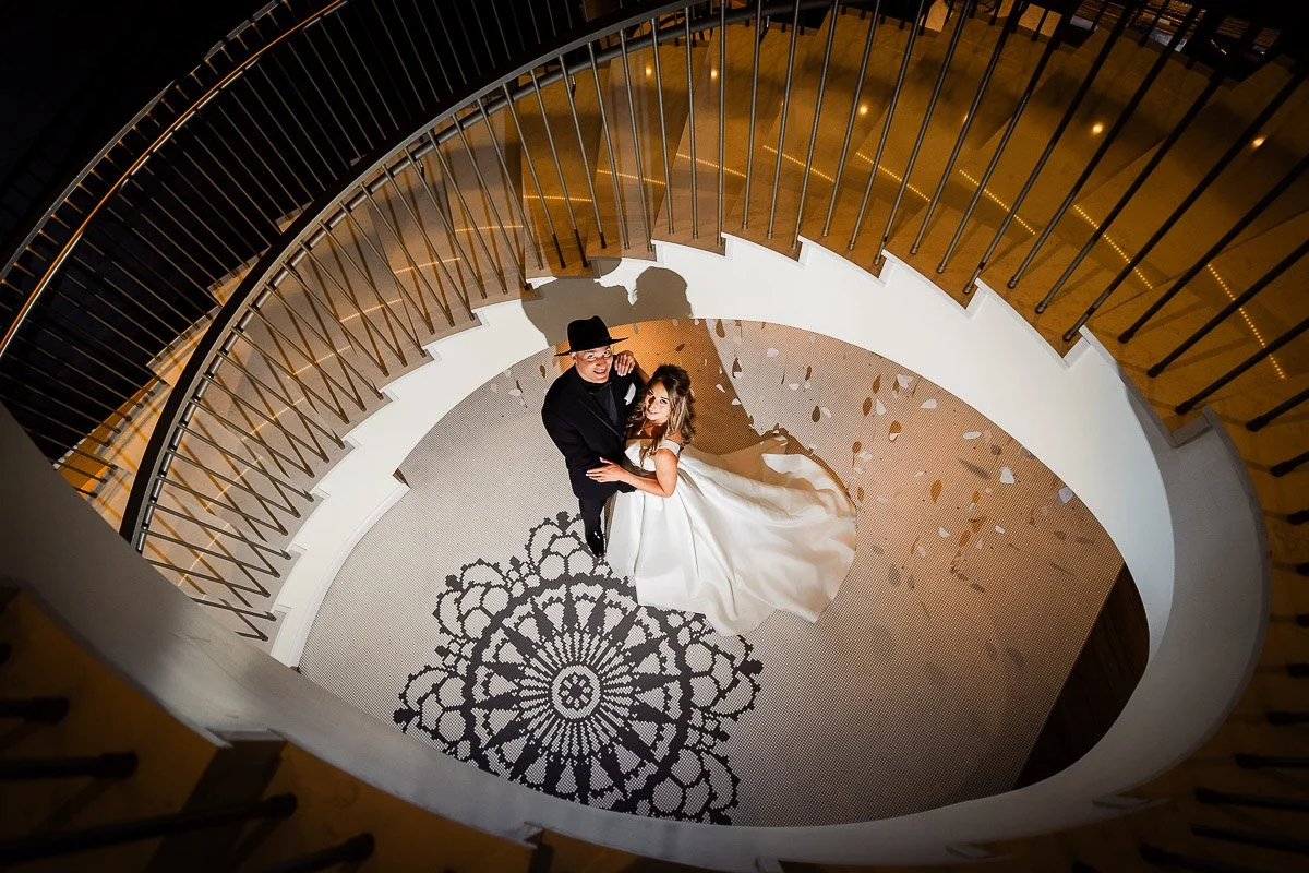 A couple stands on an ornate floor, viewed from above during an Elizabeth Hotel wedding in Fort Collins. They embrace in a spiral staircase, casting shadows. The setting feels romantic and elegant 