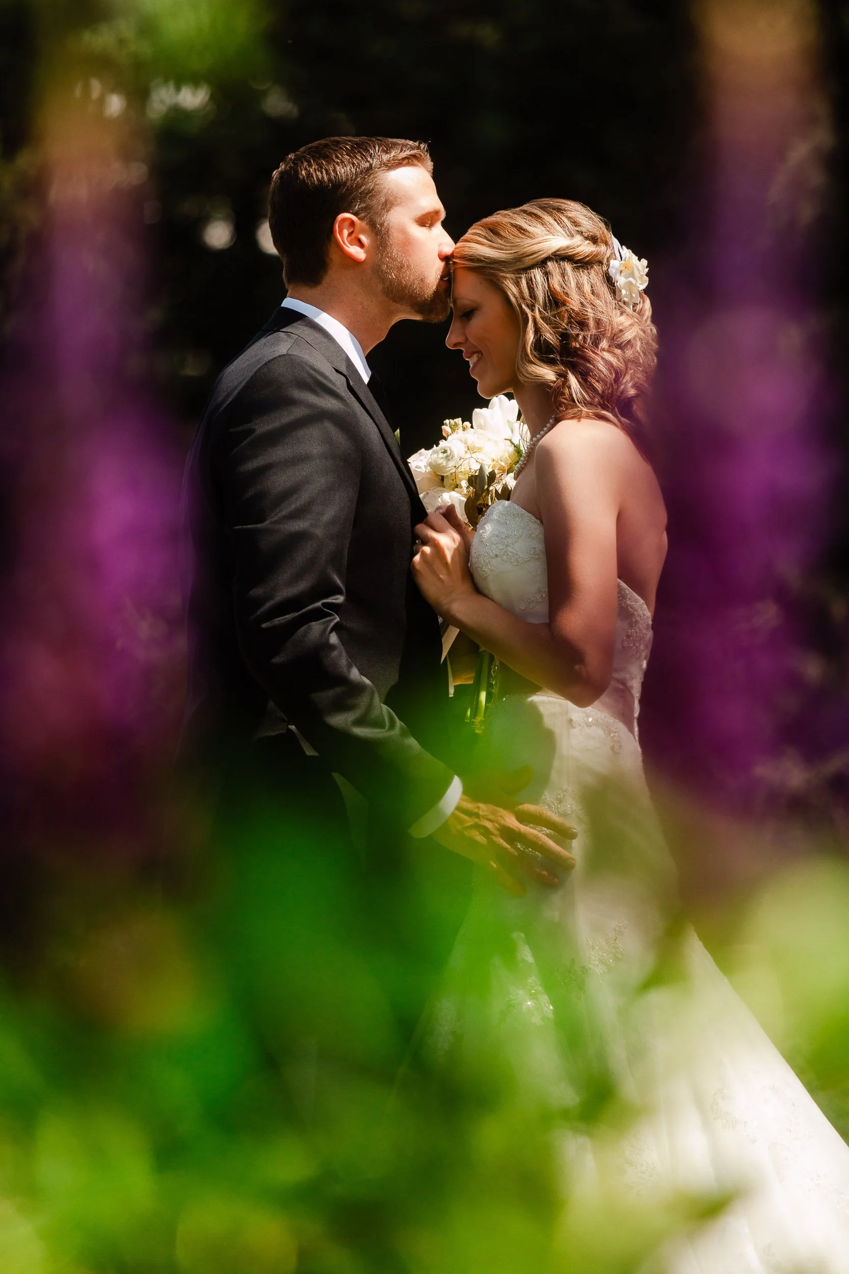 Wedding groom kisses bride on forehead among Colorado summer wildflowers in Vail during a Donovan Pavilion wedding.