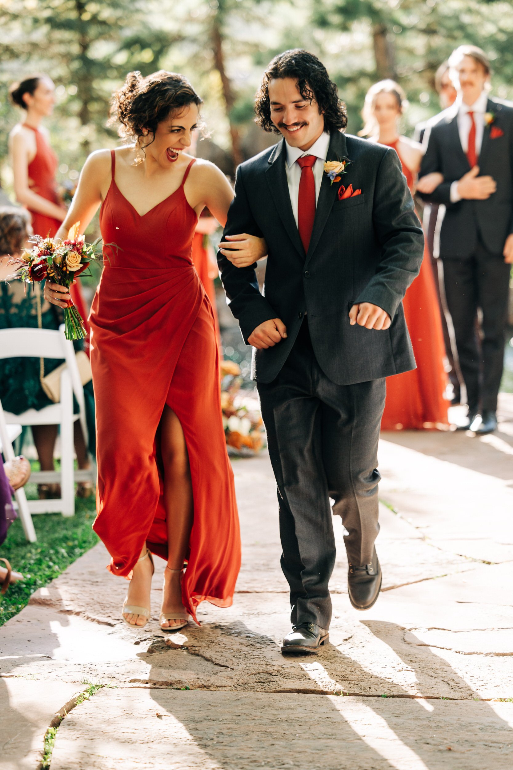 A bridesmaid wearing a red dress laughs walking down the aisle during the recessional in a Greenbriar Inn wedding in Boulder, Colorado