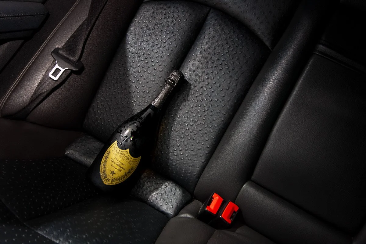A bottle of champagne rests on a luxurious, textured leather car seat. The lighting casts a dramatic shadow, highlighting the bottle's elegant label.